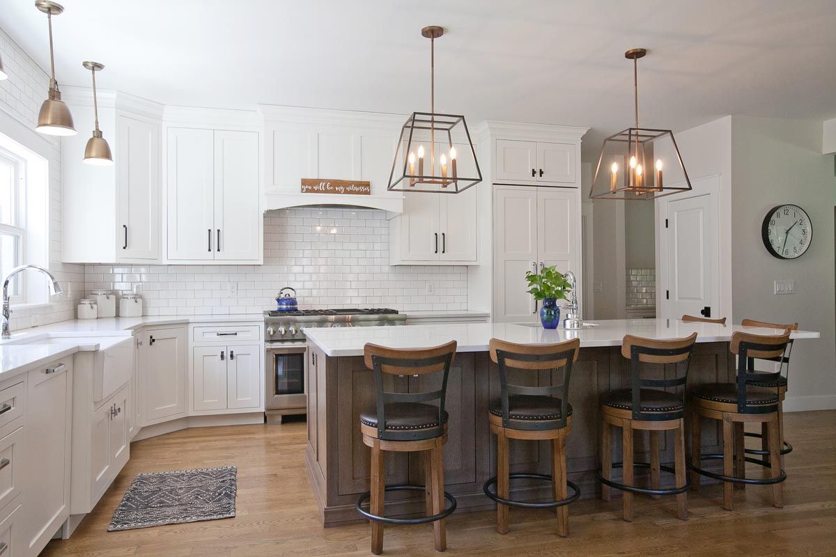 A kitchen with white cabinets, wooden floors, stools, and a large island.