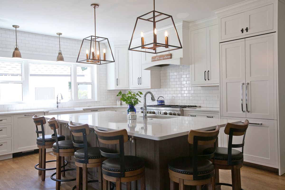A kitchen with white cabinets, granite counter tops, stools, and a large island.