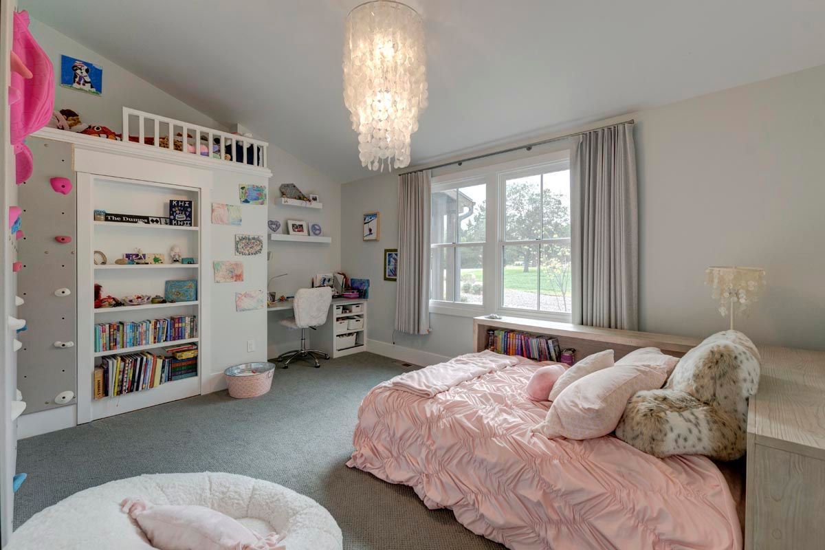 A bedroom with a bed, desk, shelves, and a chandelier.