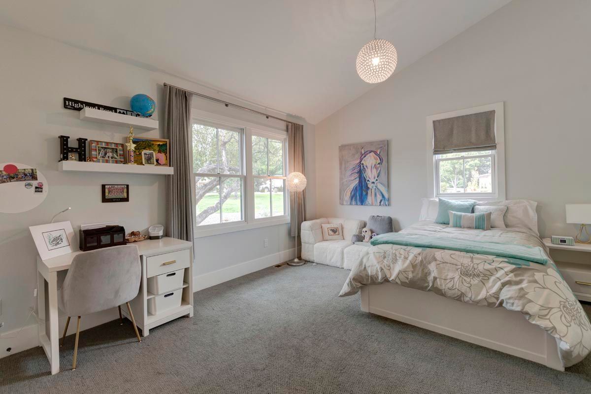 A bedroom with a bed, desk, couch, and window.