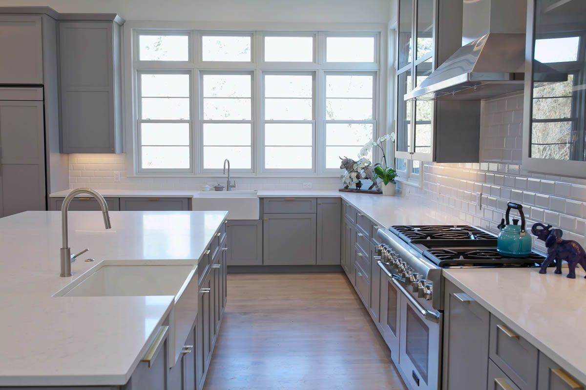 A kitchen with gray cabinets, white counter tops, a stove, and a sink.
