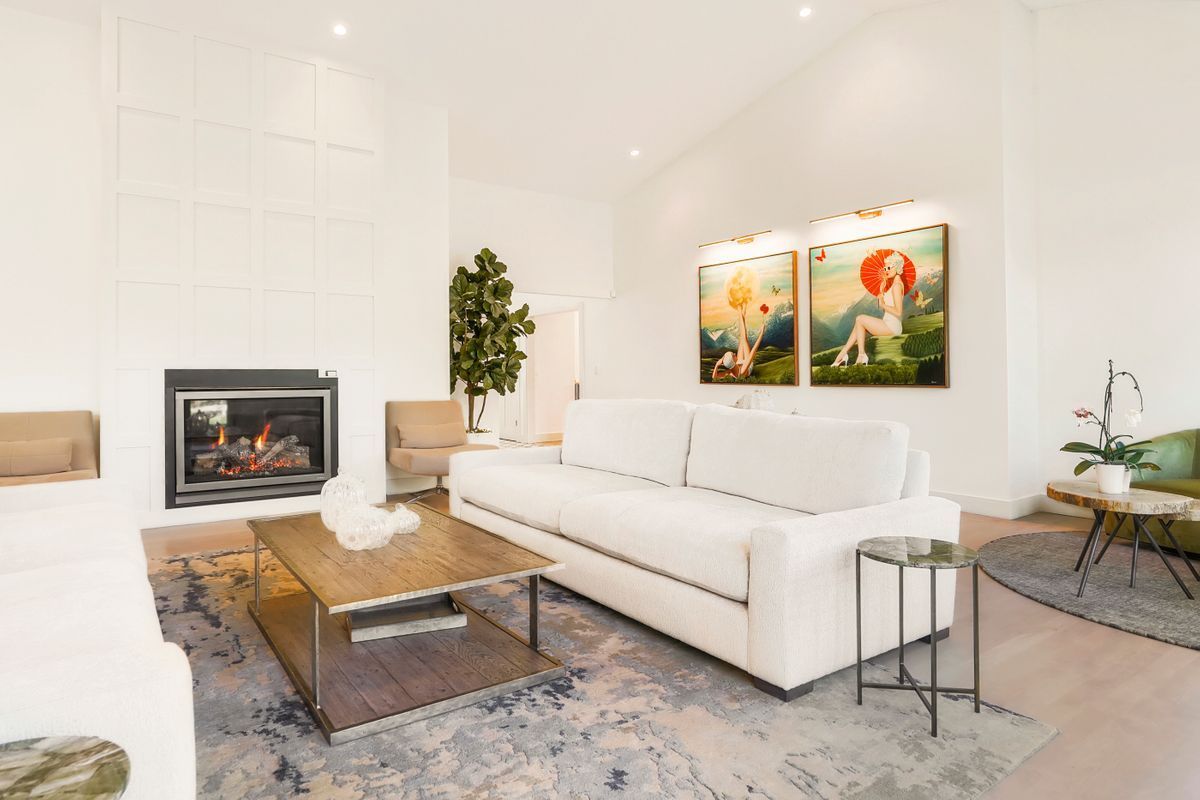 A living room with a white couch, coffee table, fireplace, and paintings on the wall.