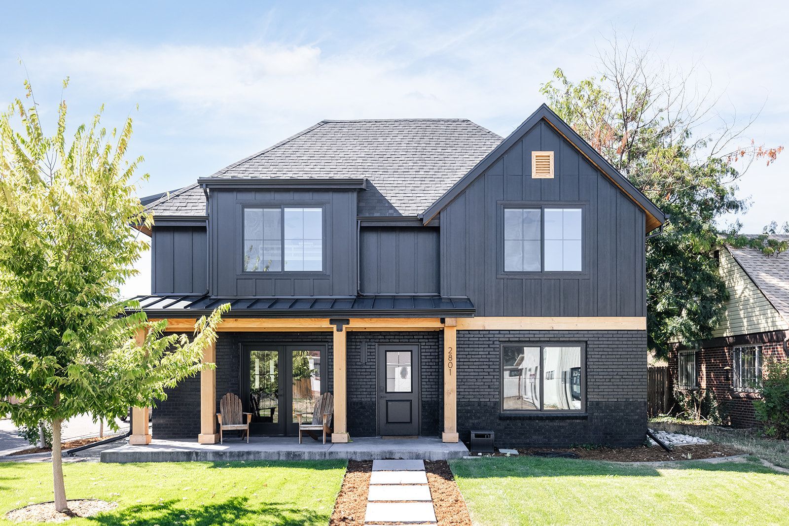 A black house with a wooden porch is sitting on top of a lush green lawn.