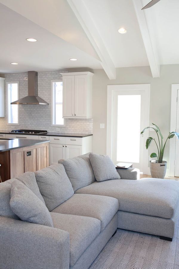 A living room with a sectional couch and a kitchen in the background.
