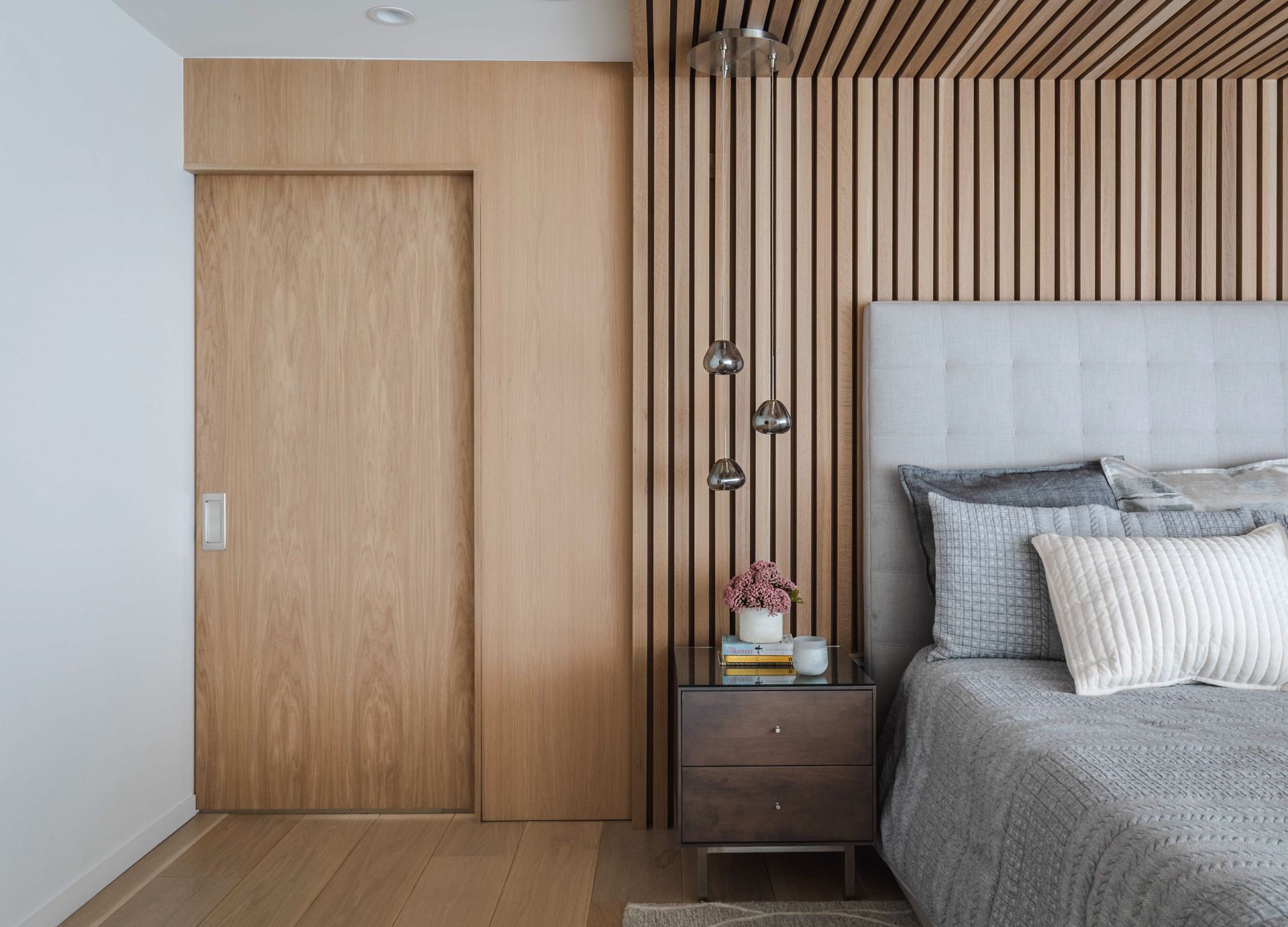 A bedroom with a bed , nightstand , and wooden wall.