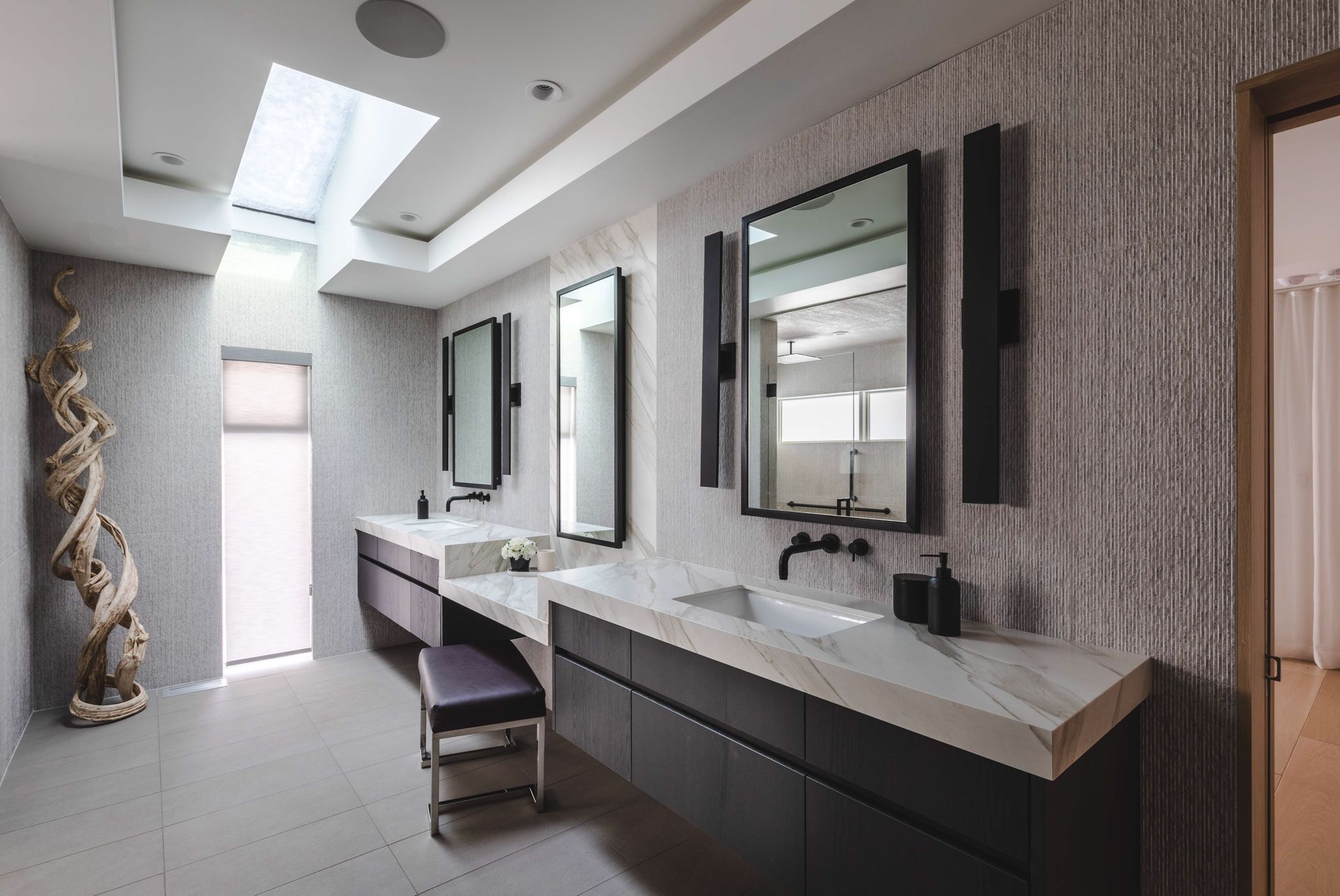 A bathroom with two sinks, two mirrors and a bench.