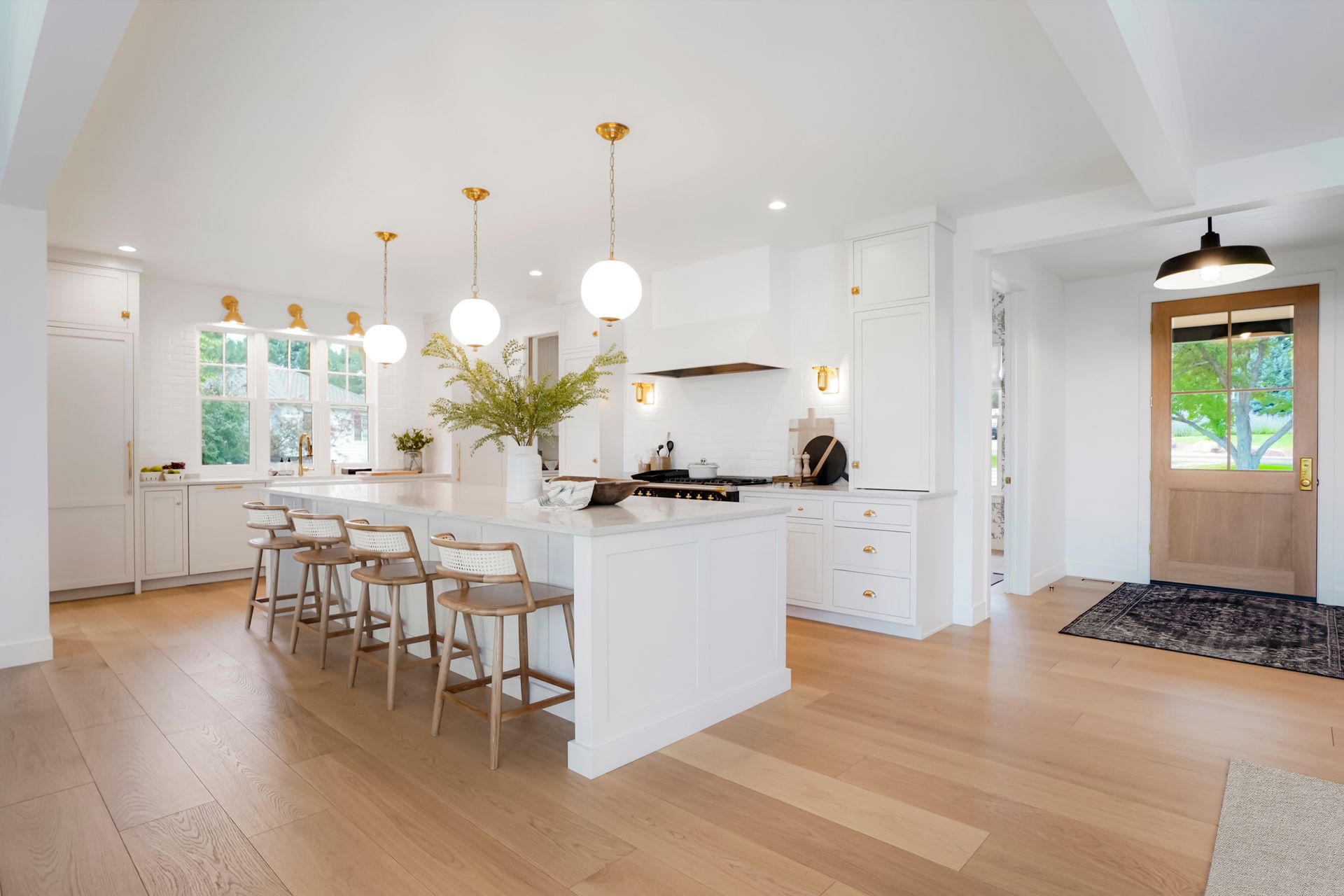 A kitchen with white cabinets , wooden floors , stools and a large island.