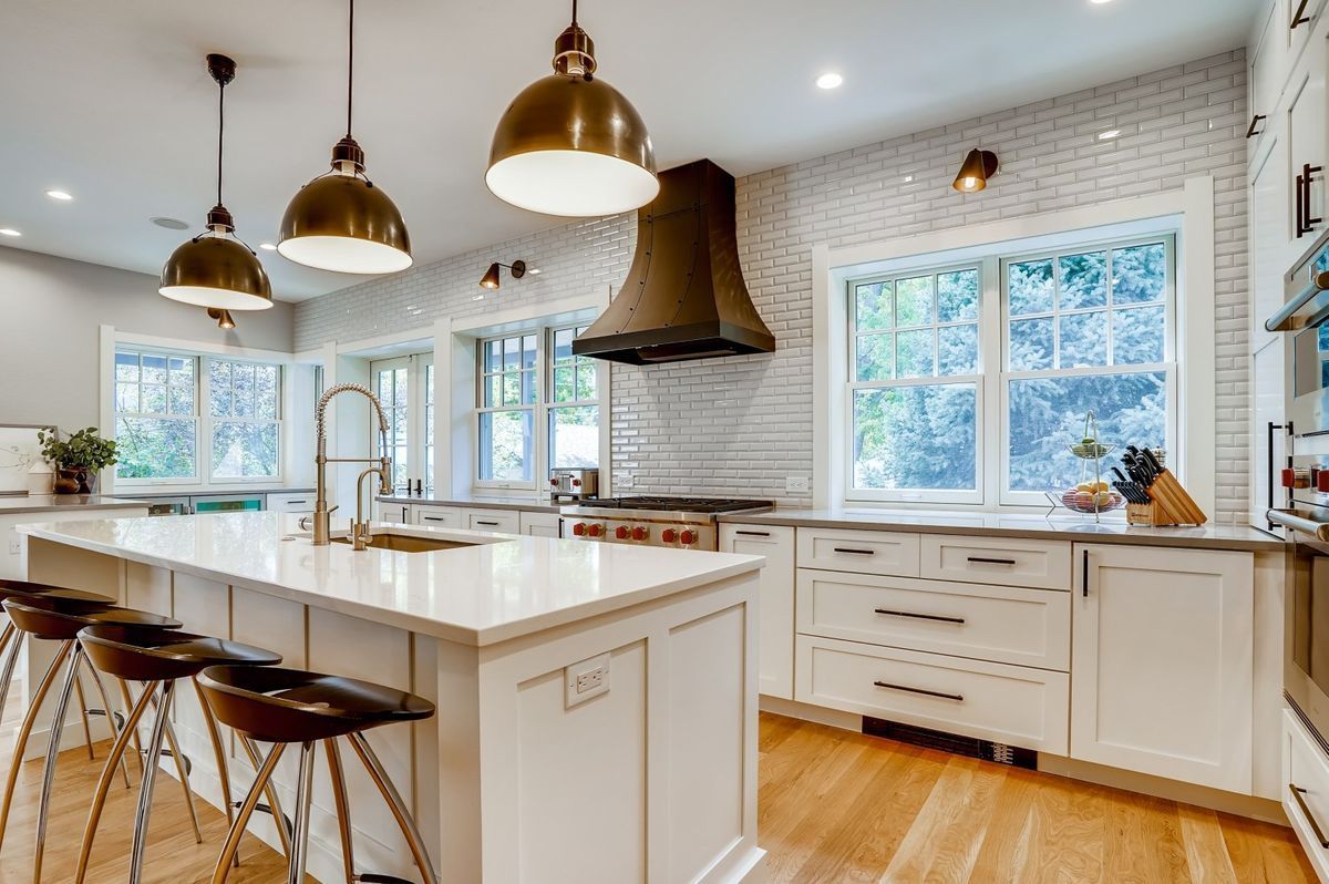 A kitchen with white cabinets, stools, a large island and a stove.