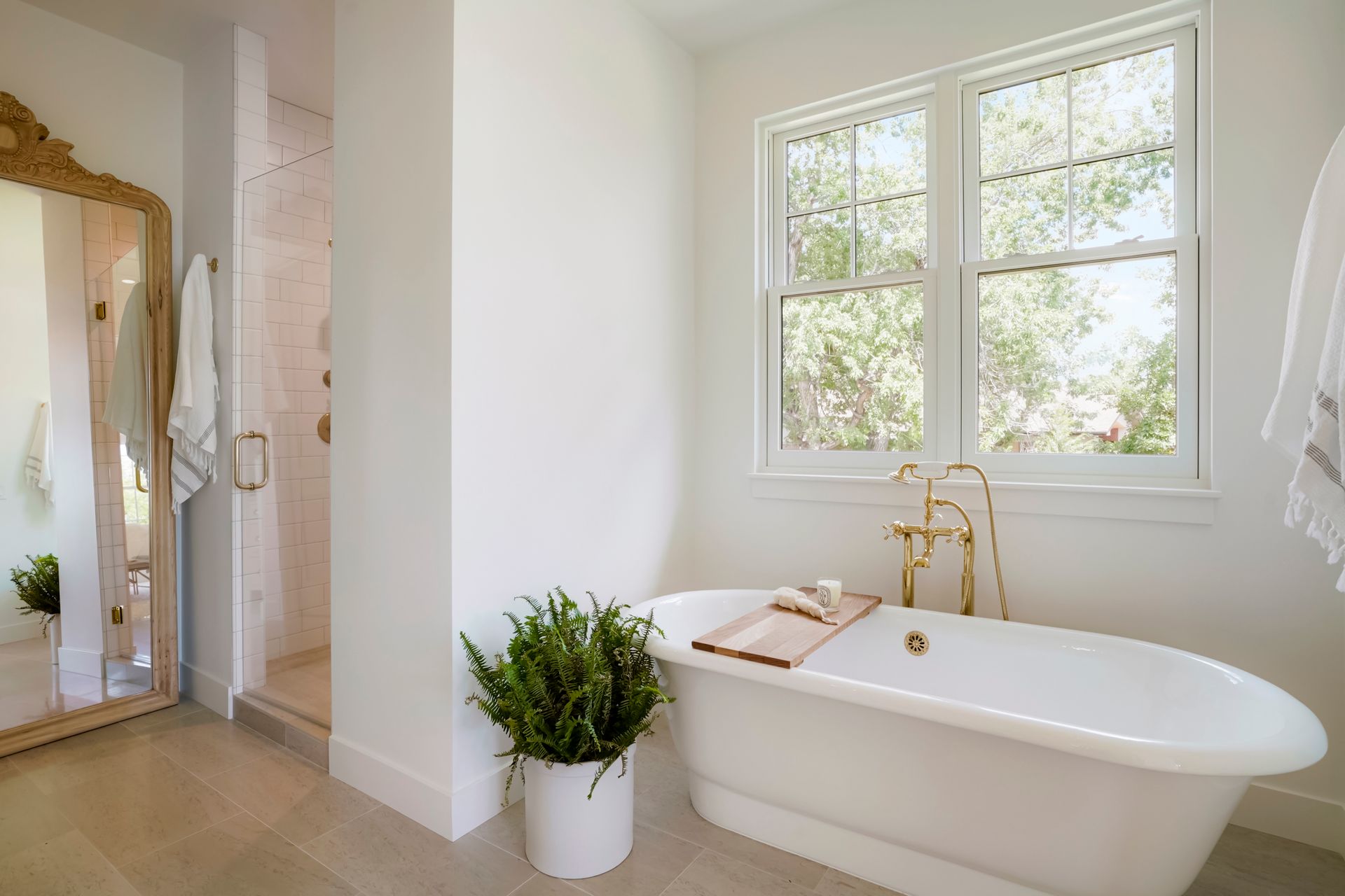 A bathroom with a tub , shower , mirror and window.