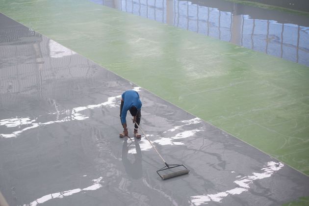 Person washing a wet concrete surface with a squeegee near a pool