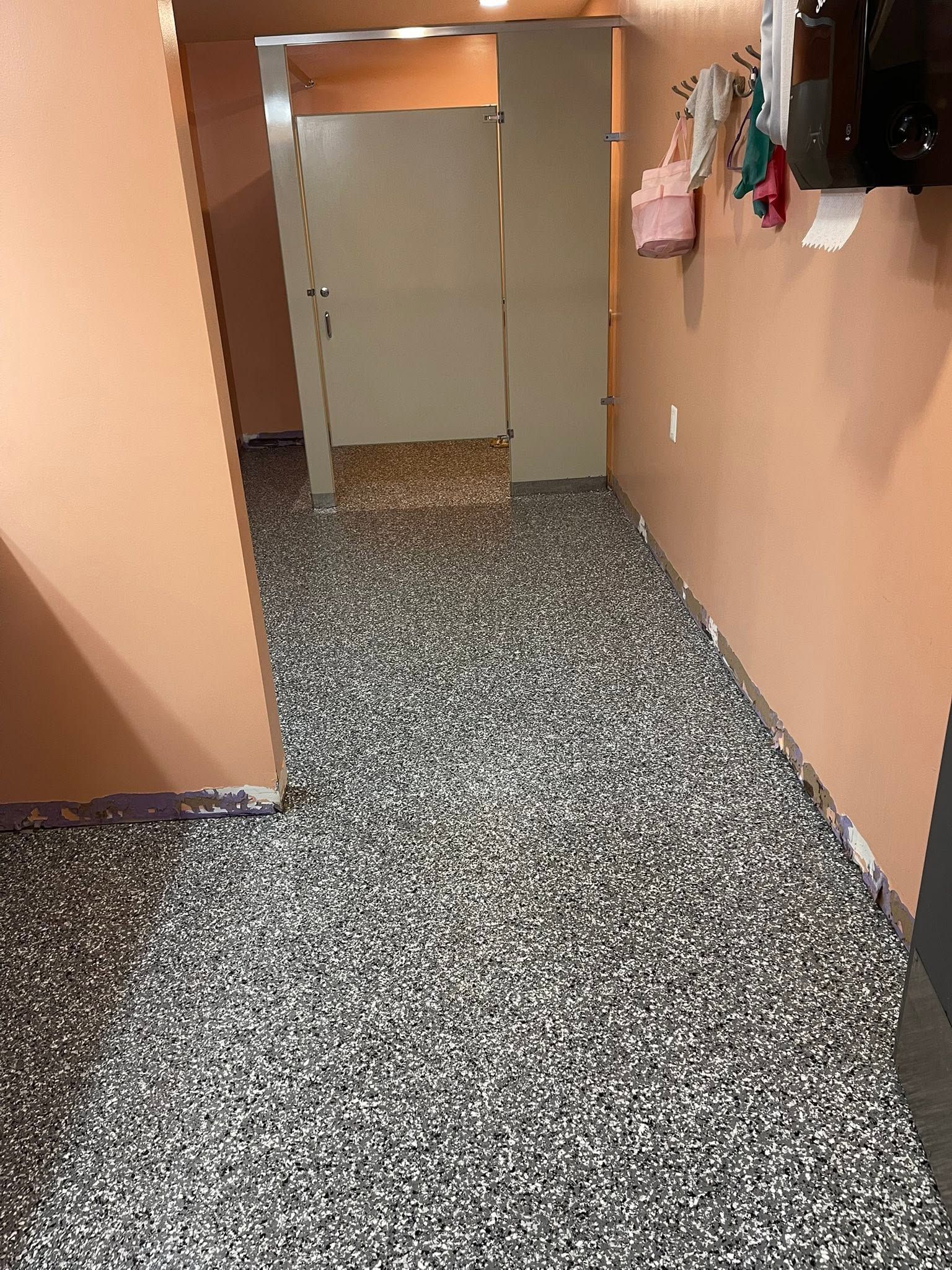 Narrow hallway with peach walls and speckled carpet, leading to a doorway with hanging clothes on the right.