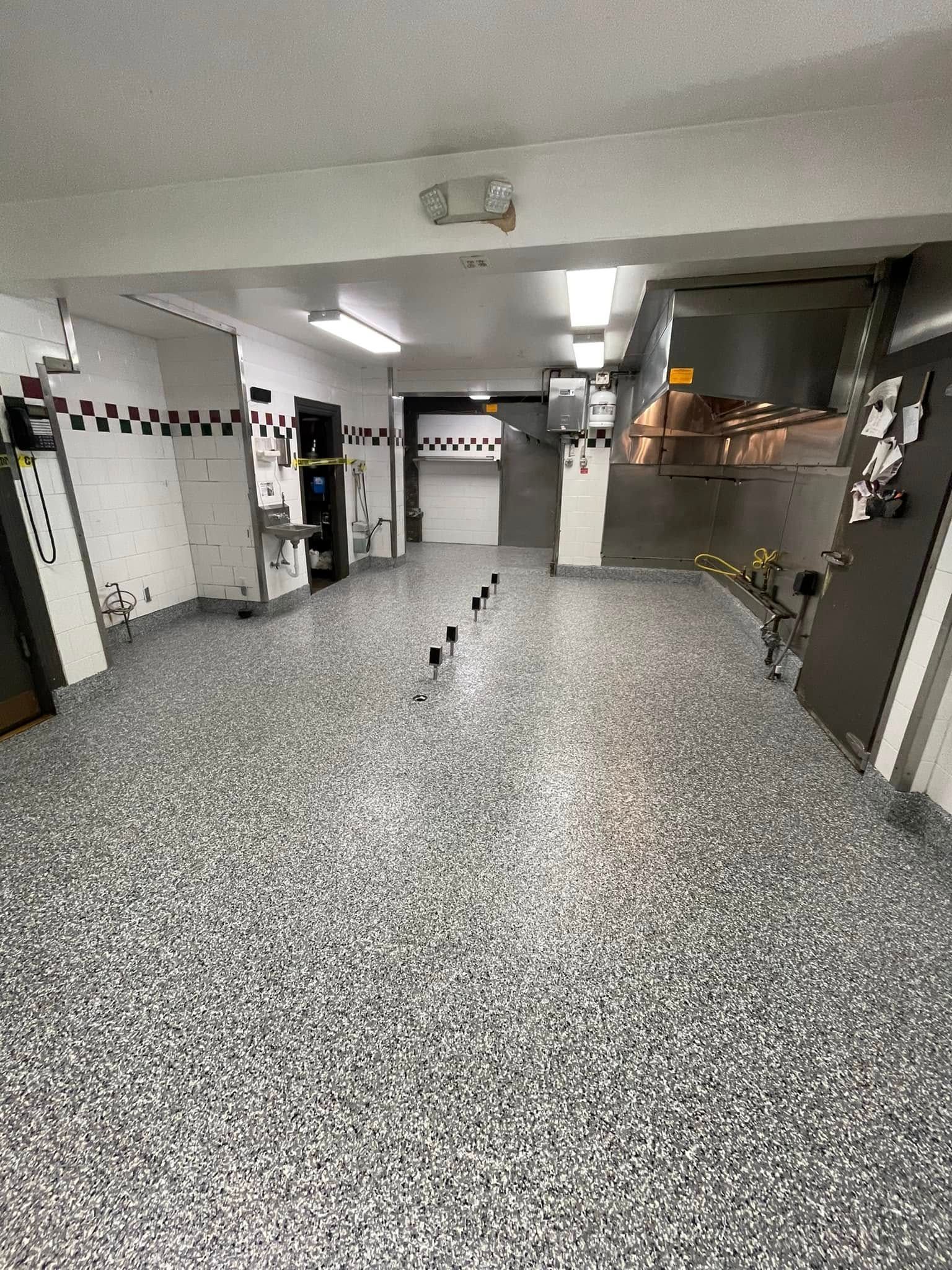Wide indoor hallway with speckled floor, tiled walls, and fluorescent lights, leading to a room at the end