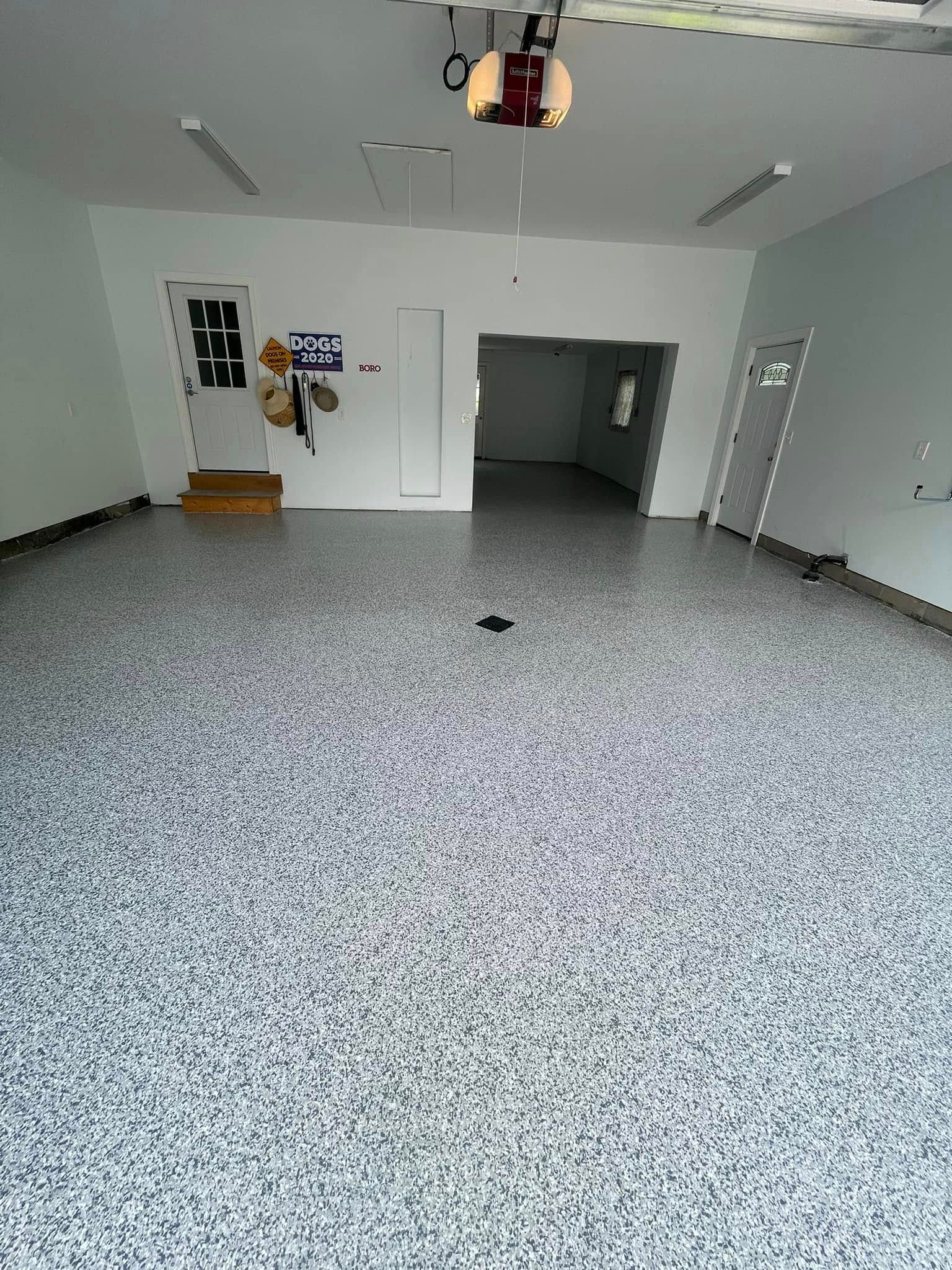 Empty speckled-floor room with white walls, open doorway, and a ceiling-mounted projector.
