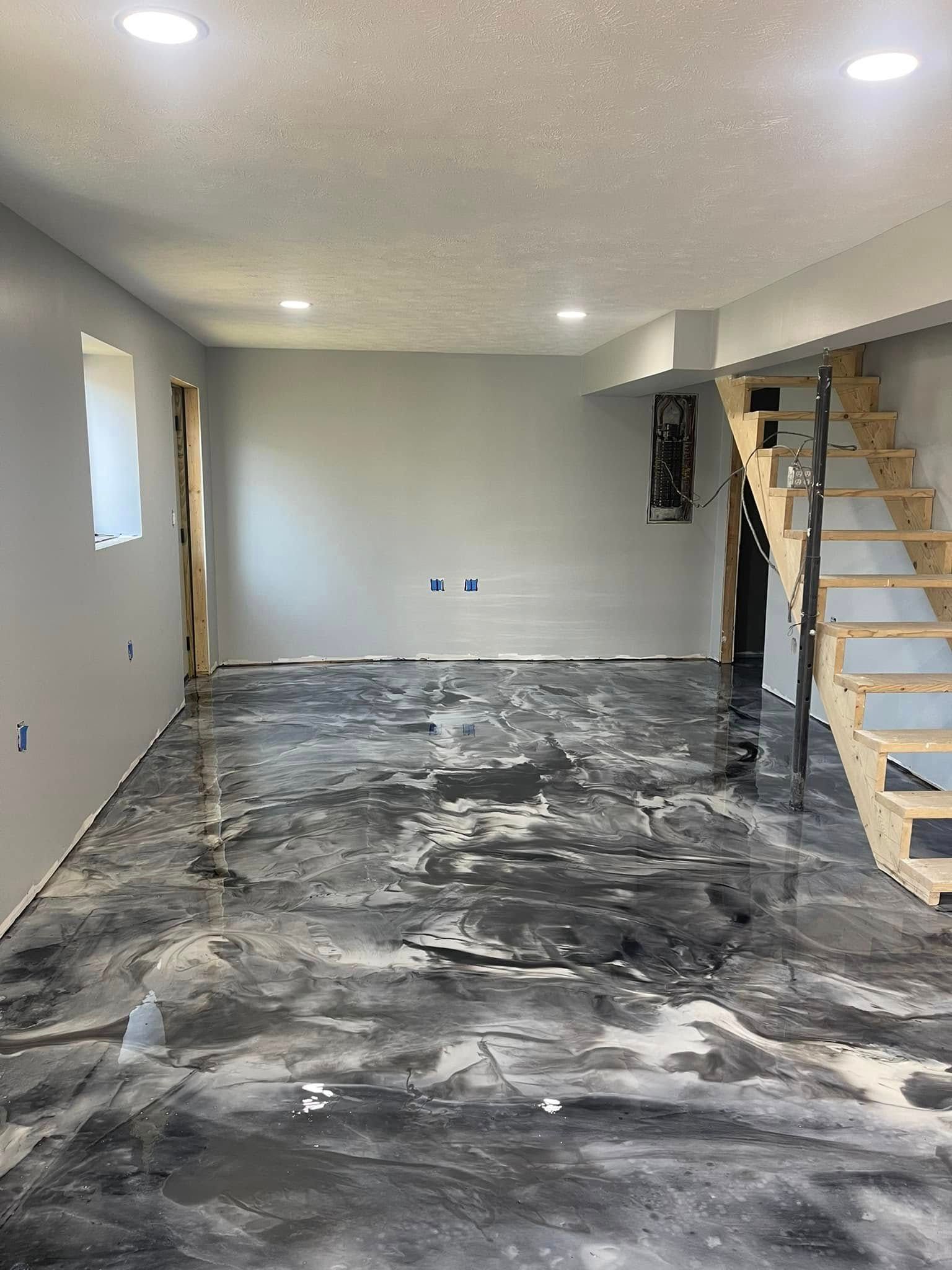 Empty basement room with unfinished concrete floor, light gray walls, and a wooden staircase on the right