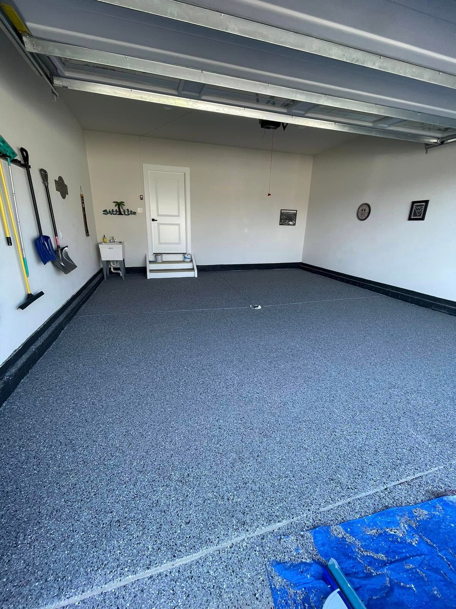 Empty garage with gray carpet, white door, wall decor, and a blue tarp in the foreground