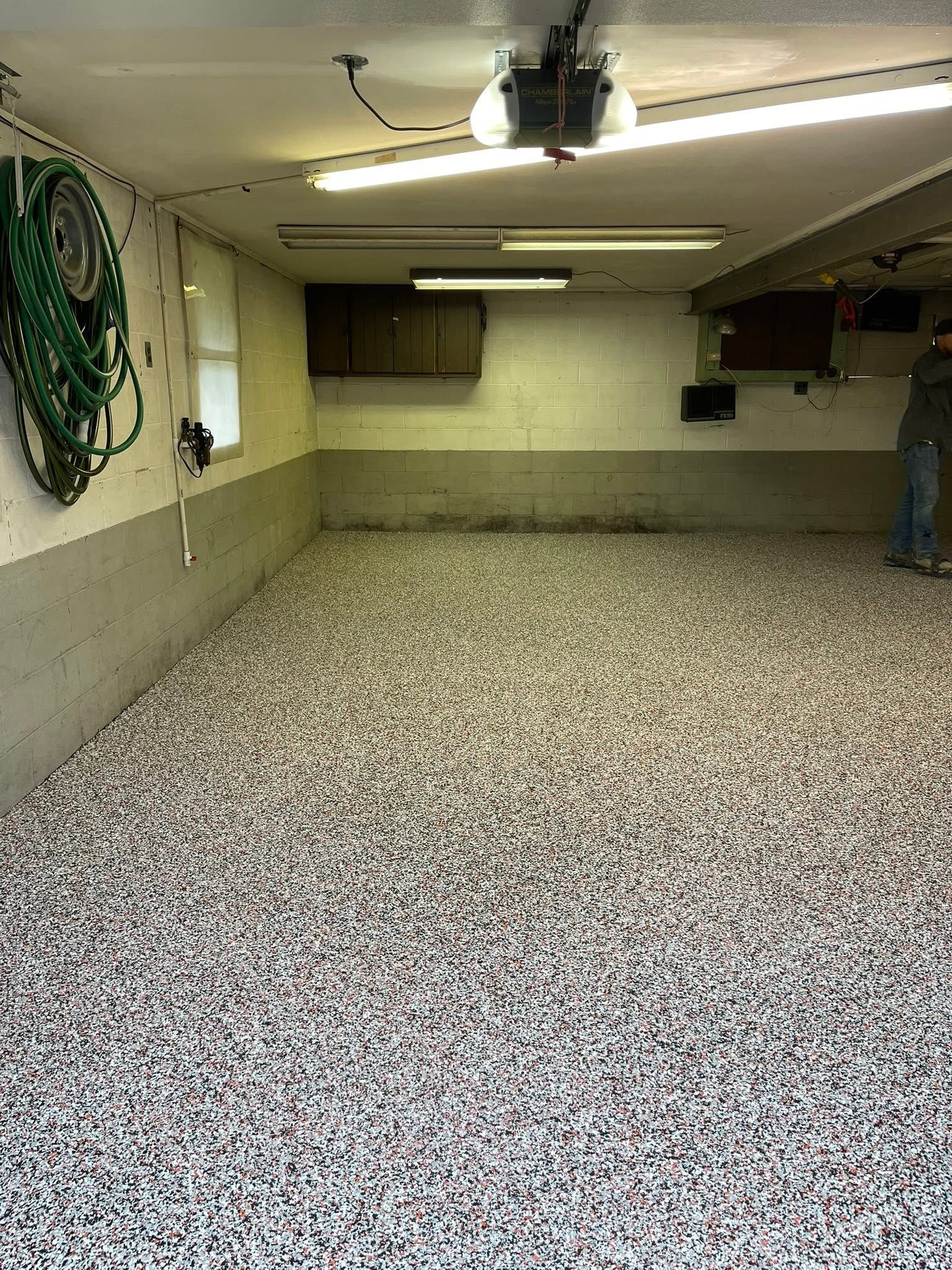 A garage with speckled epoxy floor, beige walls, ceiling lights, and a person standing at the far right.