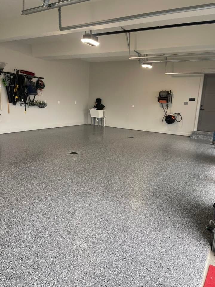 Empty garage with gray speckled floor, white walls, ceiling lights, and wall-mounted tools.
