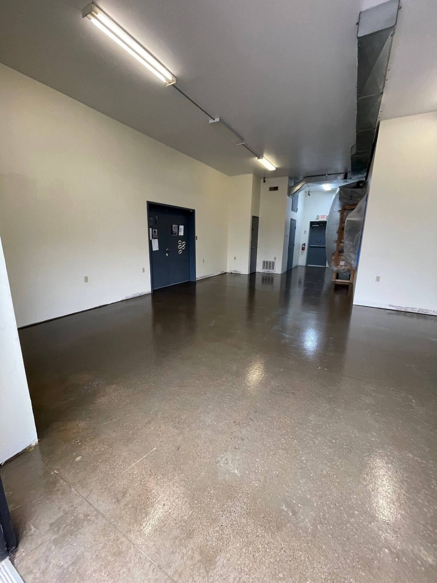 Empty indoor hallway with white walls, brown floor, and overhead fluorescent lights