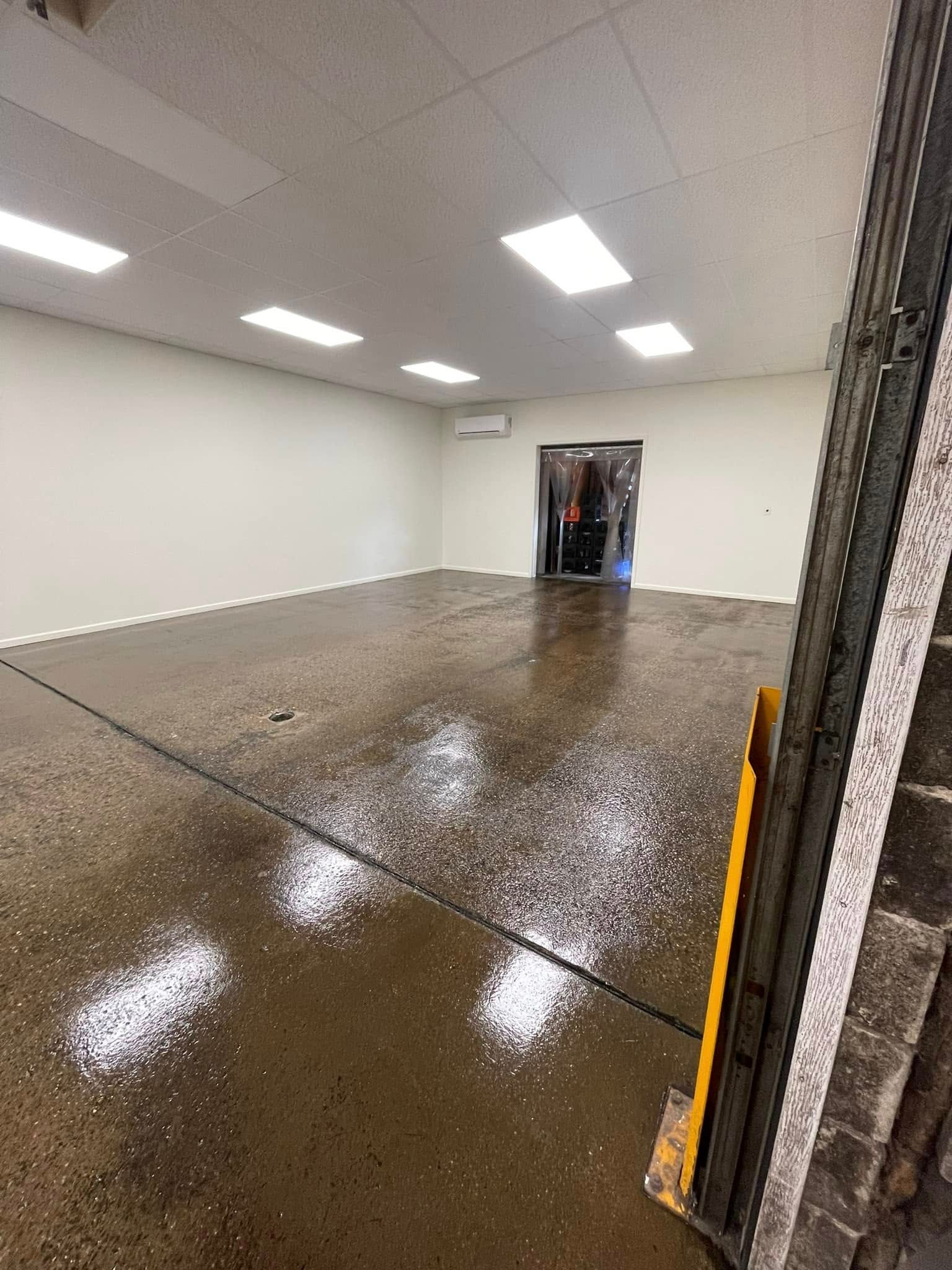 Empty white room with wet reflective floor and an open doorway in the back.