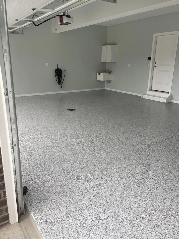 Empty garage with gray speckled floor, white walls, and a ceiling-mounted opener.