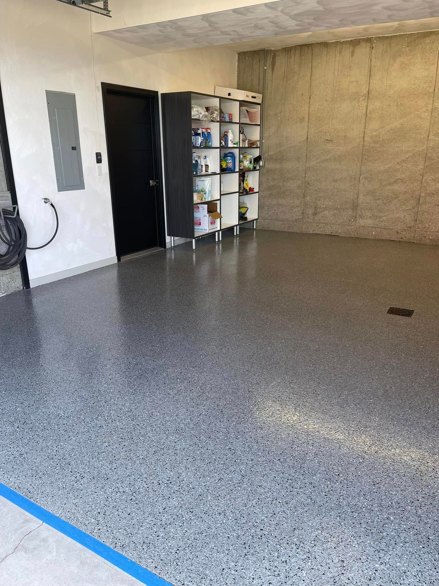 Empty garage with speckled epoxy floor, open shelving, and a workbench against the back wall.