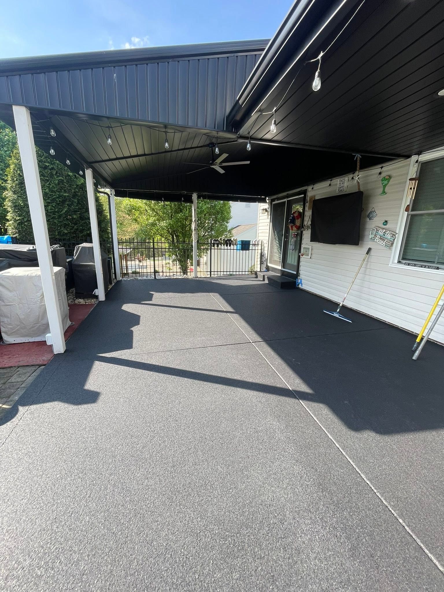 Covered driveway beside a white building, with black awning, paved ground, and a clear path to the street.