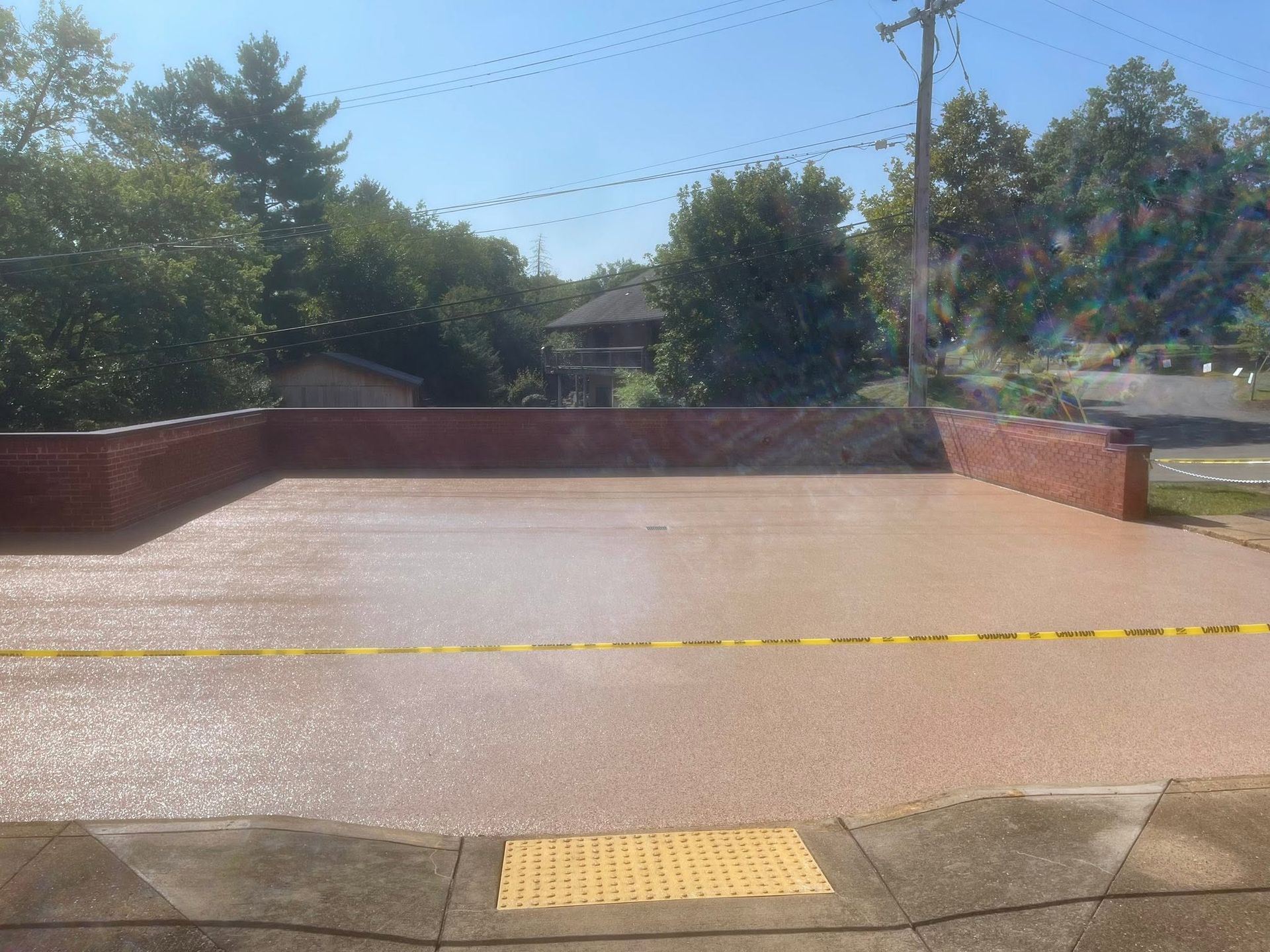 Outdoor brick terrace with a yellow tactile paving strip at the edge, trees and houses in the background