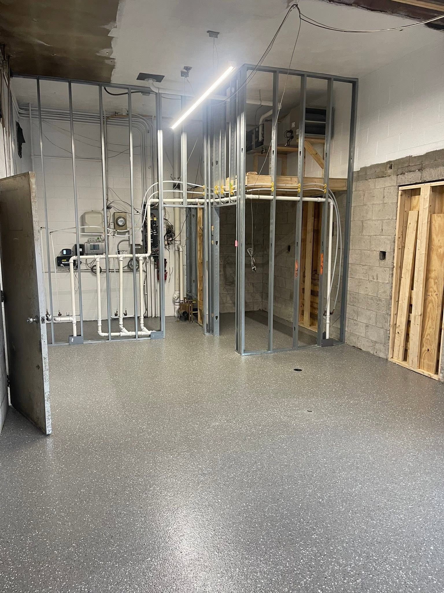 Empty unfinished room with exposed wall studs, concrete floor, and overhead fluorescent lights