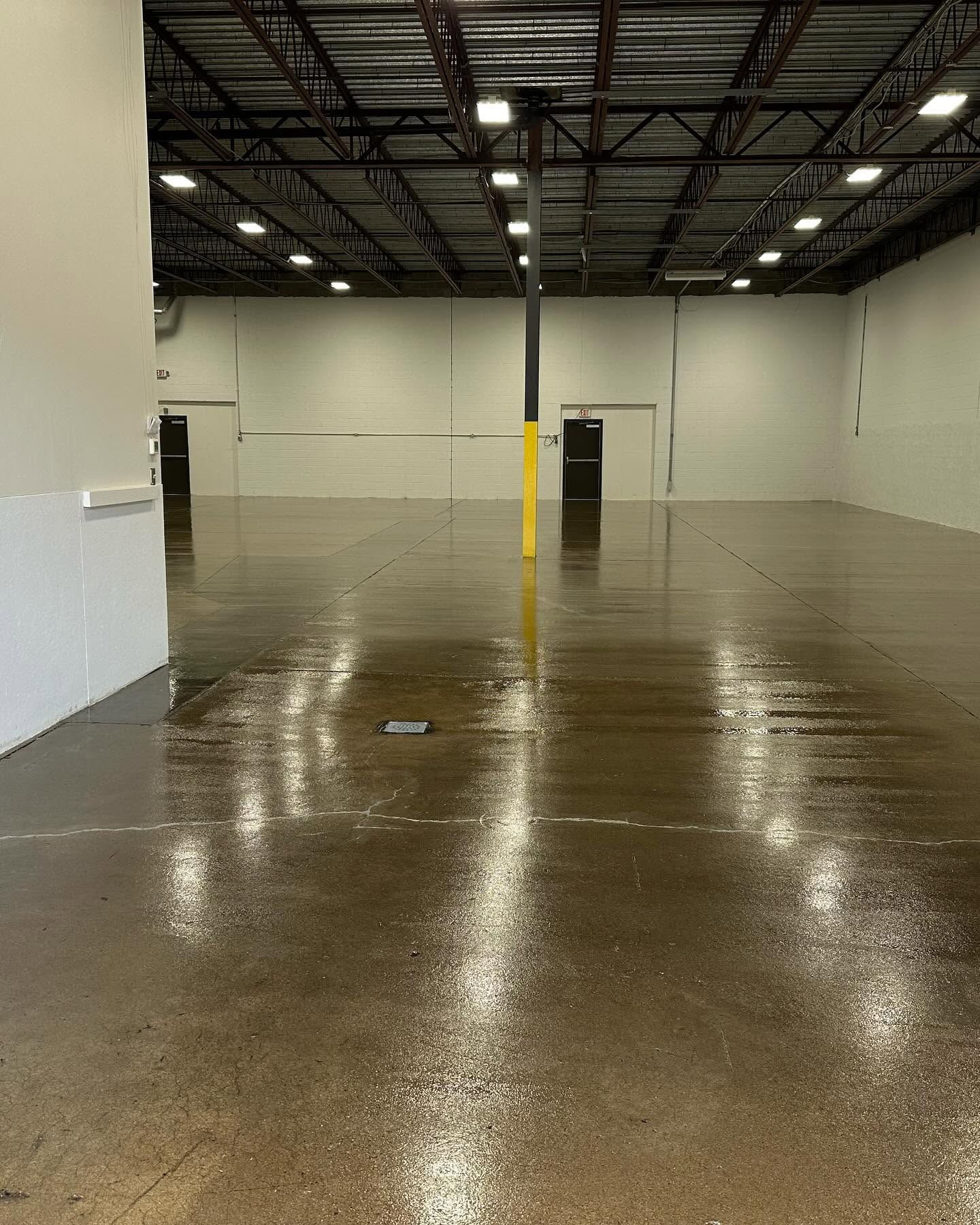 Empty indoor warehouse with wet concrete floor and white walls under overhead lights