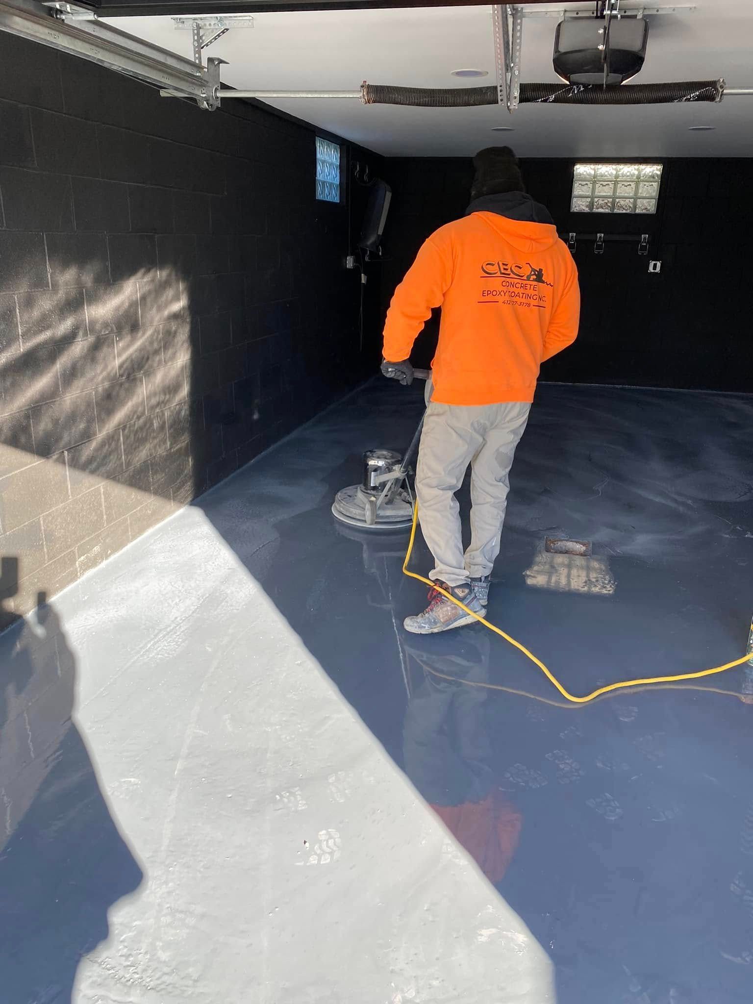 Worker in an orange shirt sanding a glossy floor inside a black-painted garage.