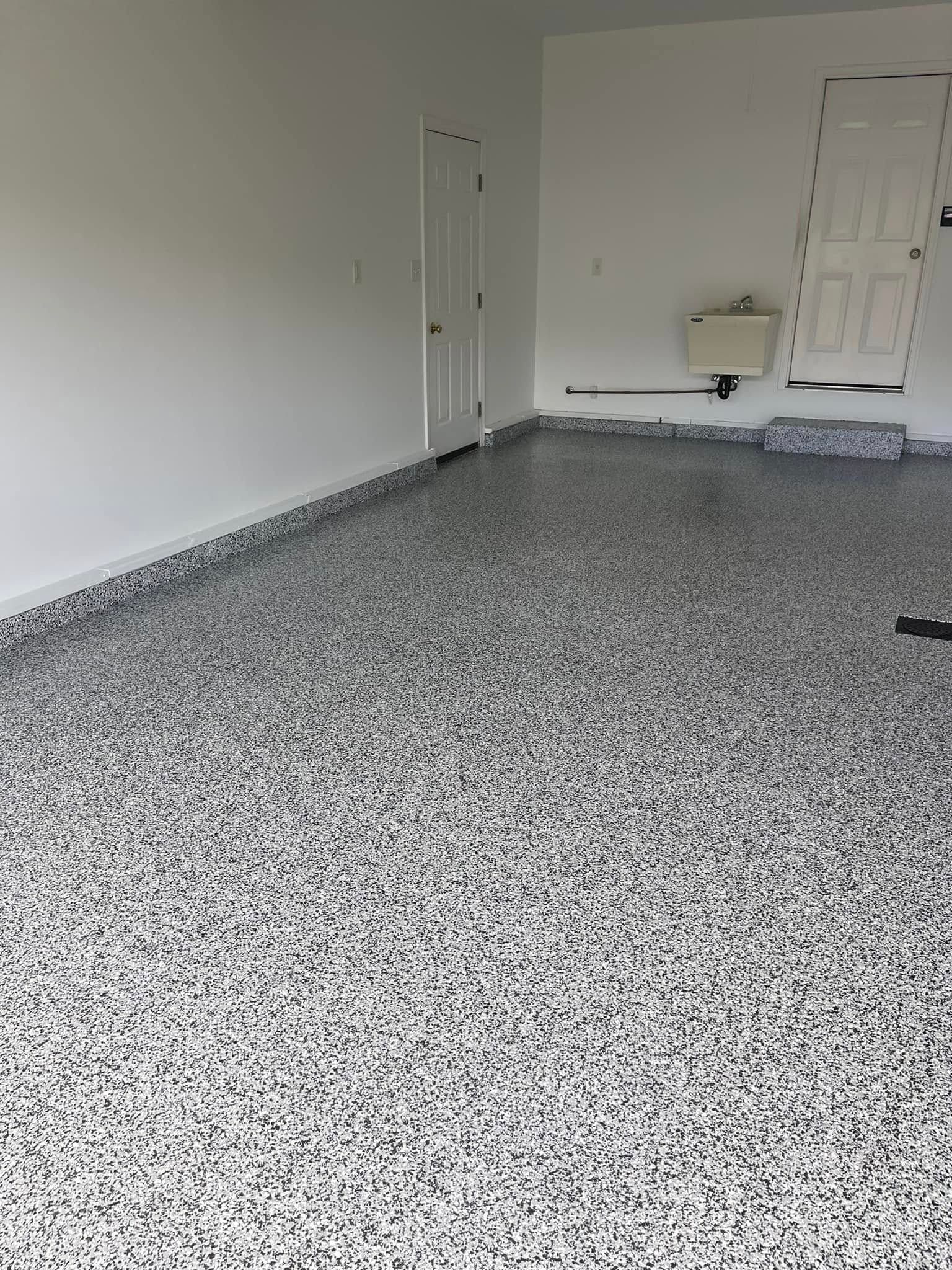 Empty room with speckled gray floor, white walls, and a wall-mounted sink near the back.