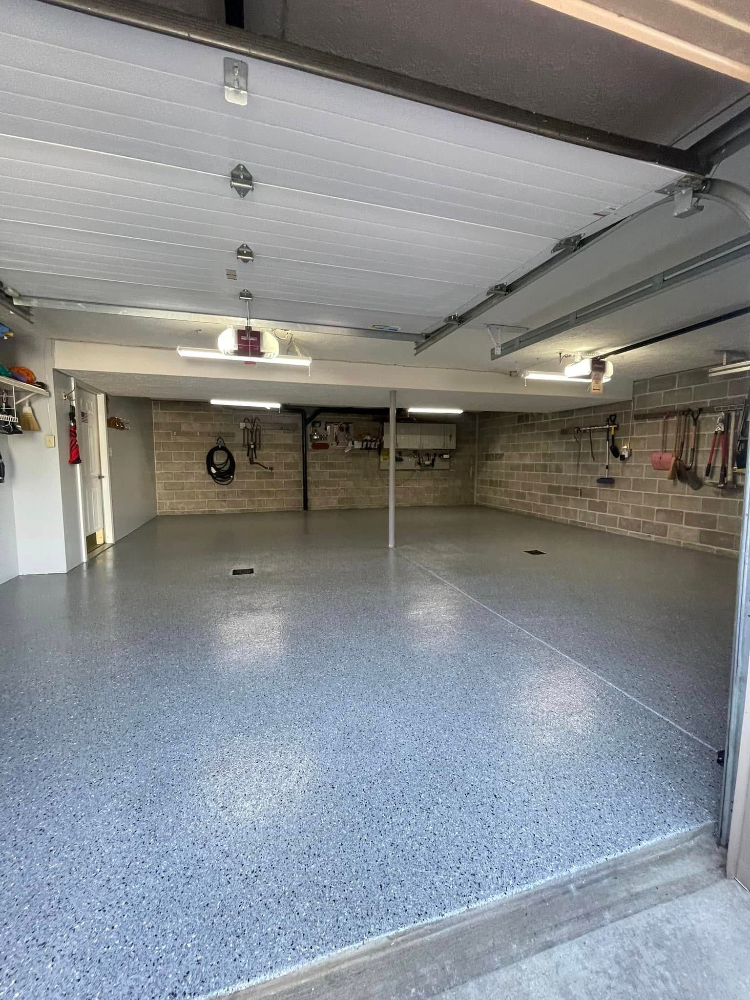 Empty garage with speckled epoxy floor, open door, and brick walls.