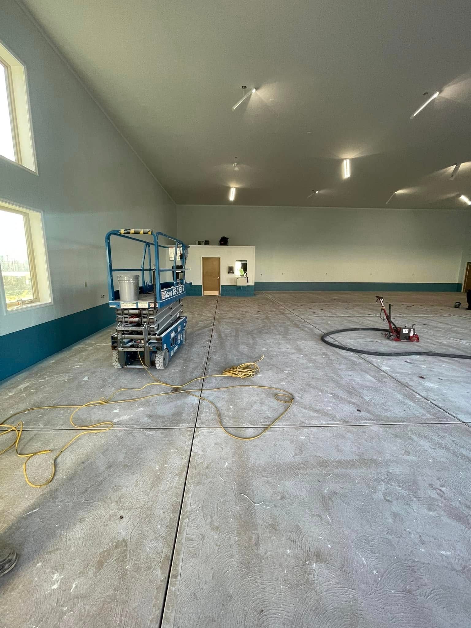 Empty warehouse with concrete floor, blue walls, overhead lights, and construction equipment inside
