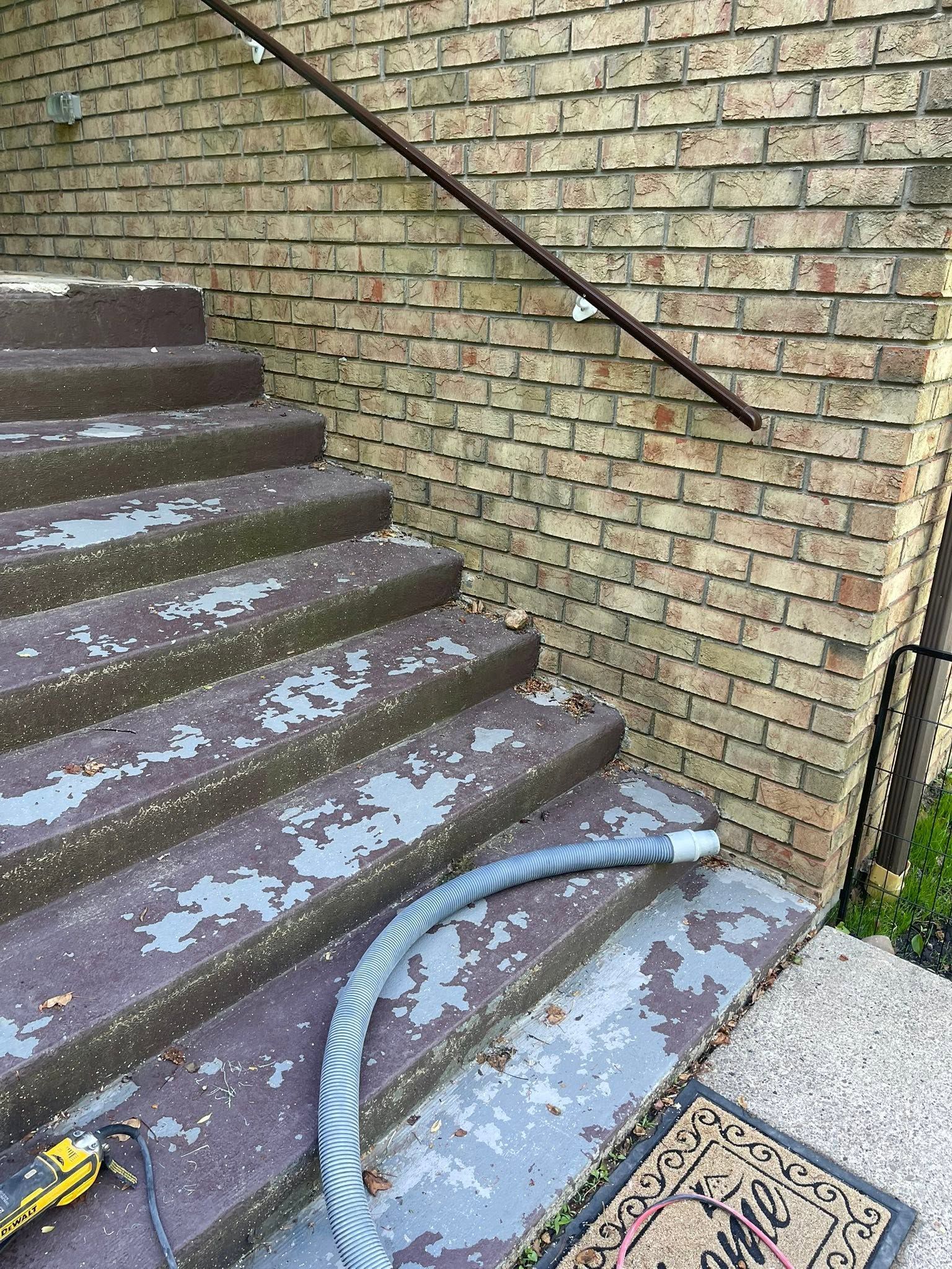 Outdoor brick stairway with icy steps, a handrail, and a hose lying across the bottom step