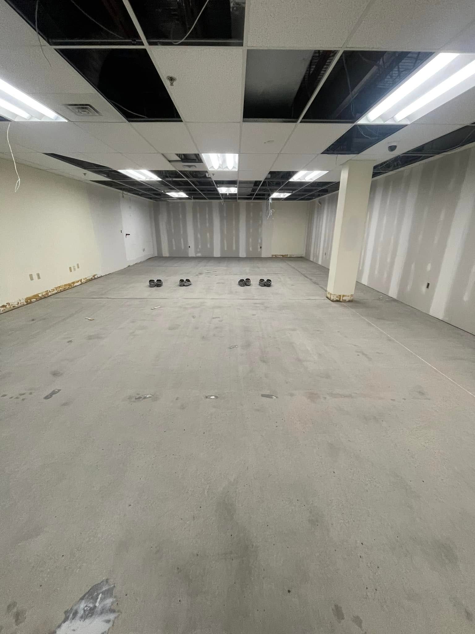 Empty unfinished office space with bare walls, concrete floor, and exposed ceiling tiles.