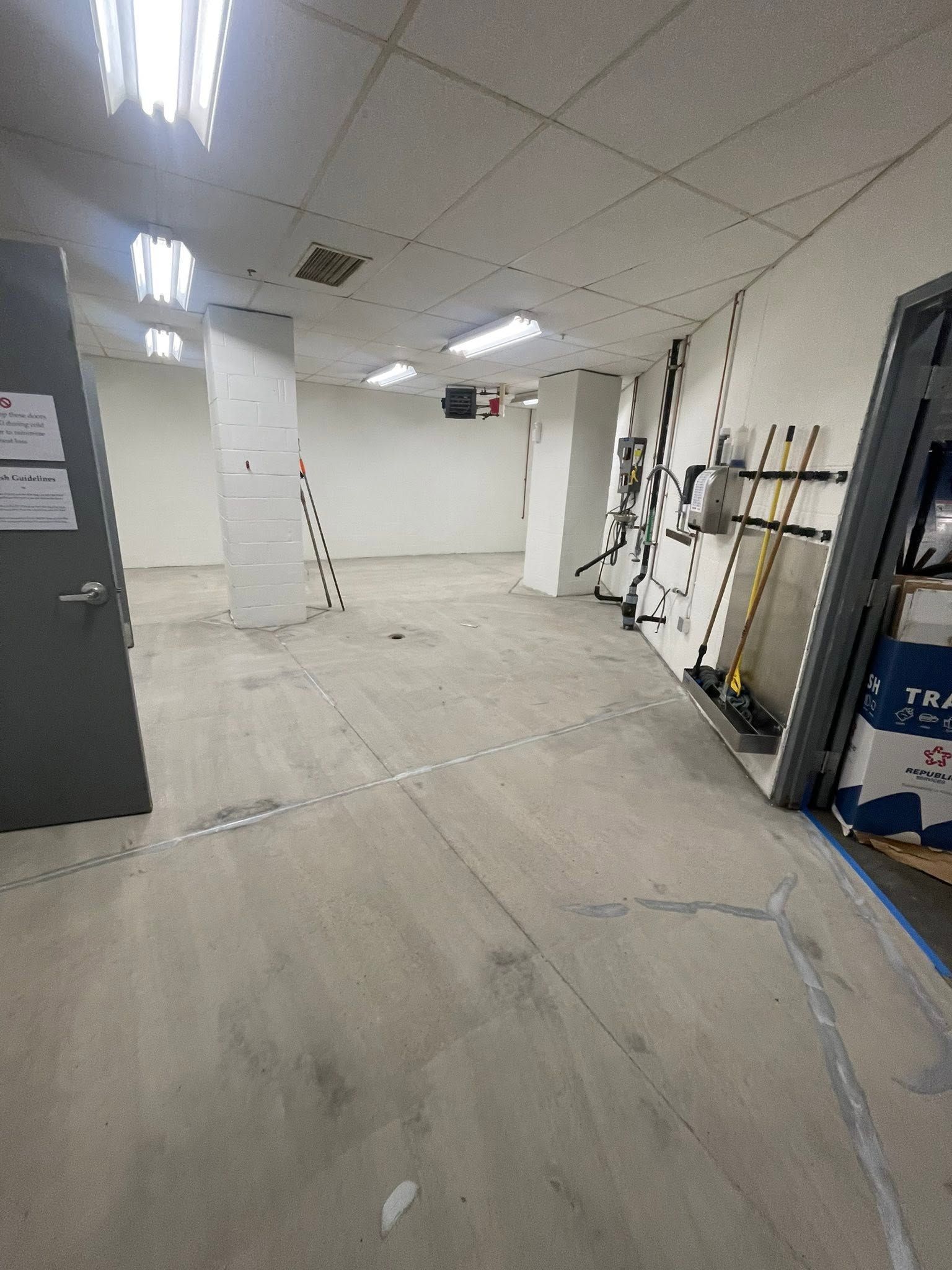 Empty unfinished room with exposed ceiling tiles, white walls, and construction materials along the sides