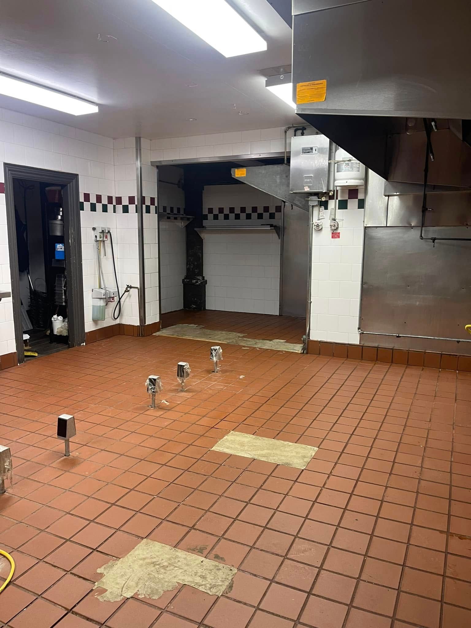 Empty commercial kitchen with red tile floor, stainless steel walls, and overhead fluorescent lights