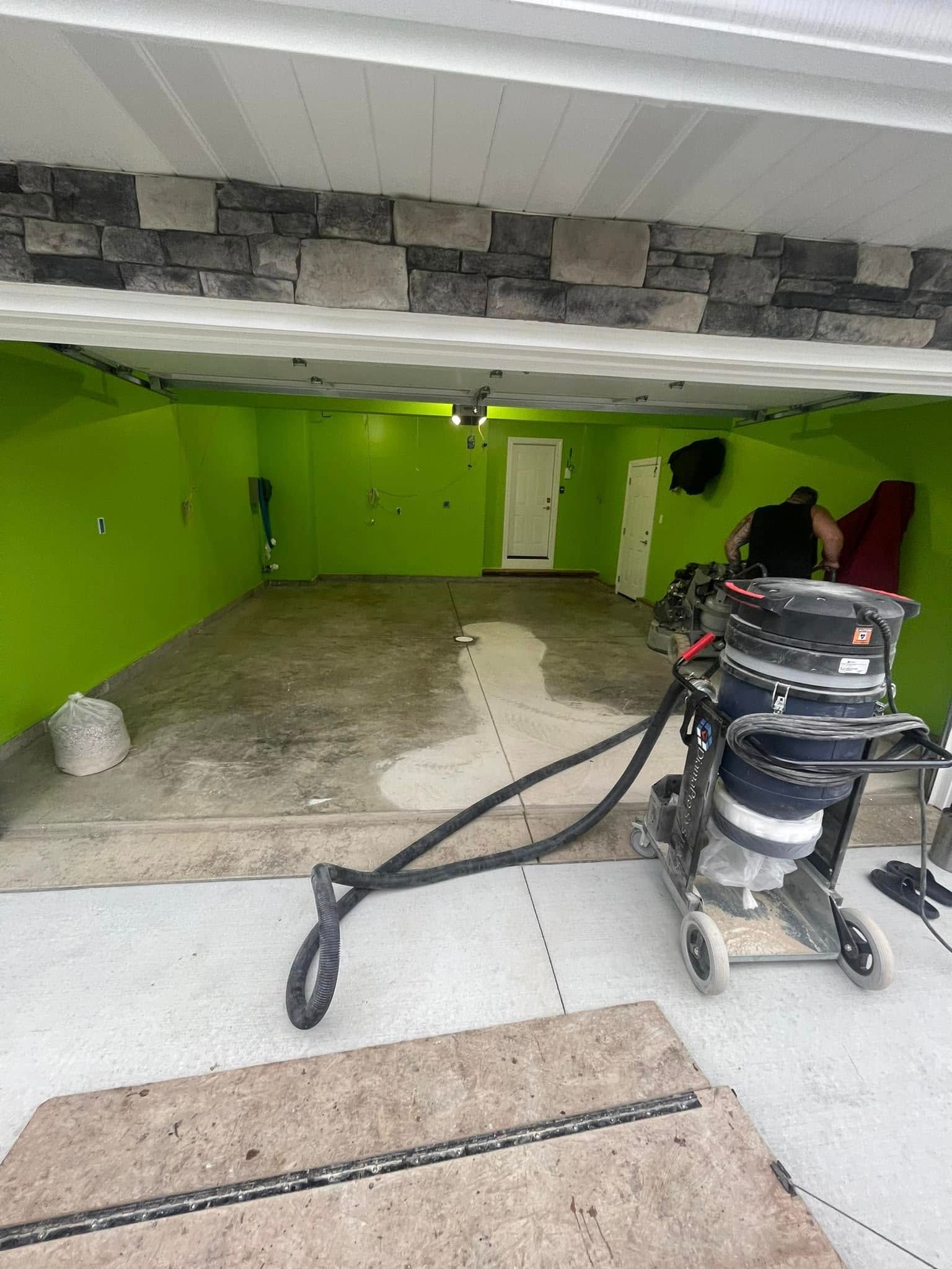 A garage interior being cleaned, with green walls, wet floor, and cleaning equipment in the foreground.