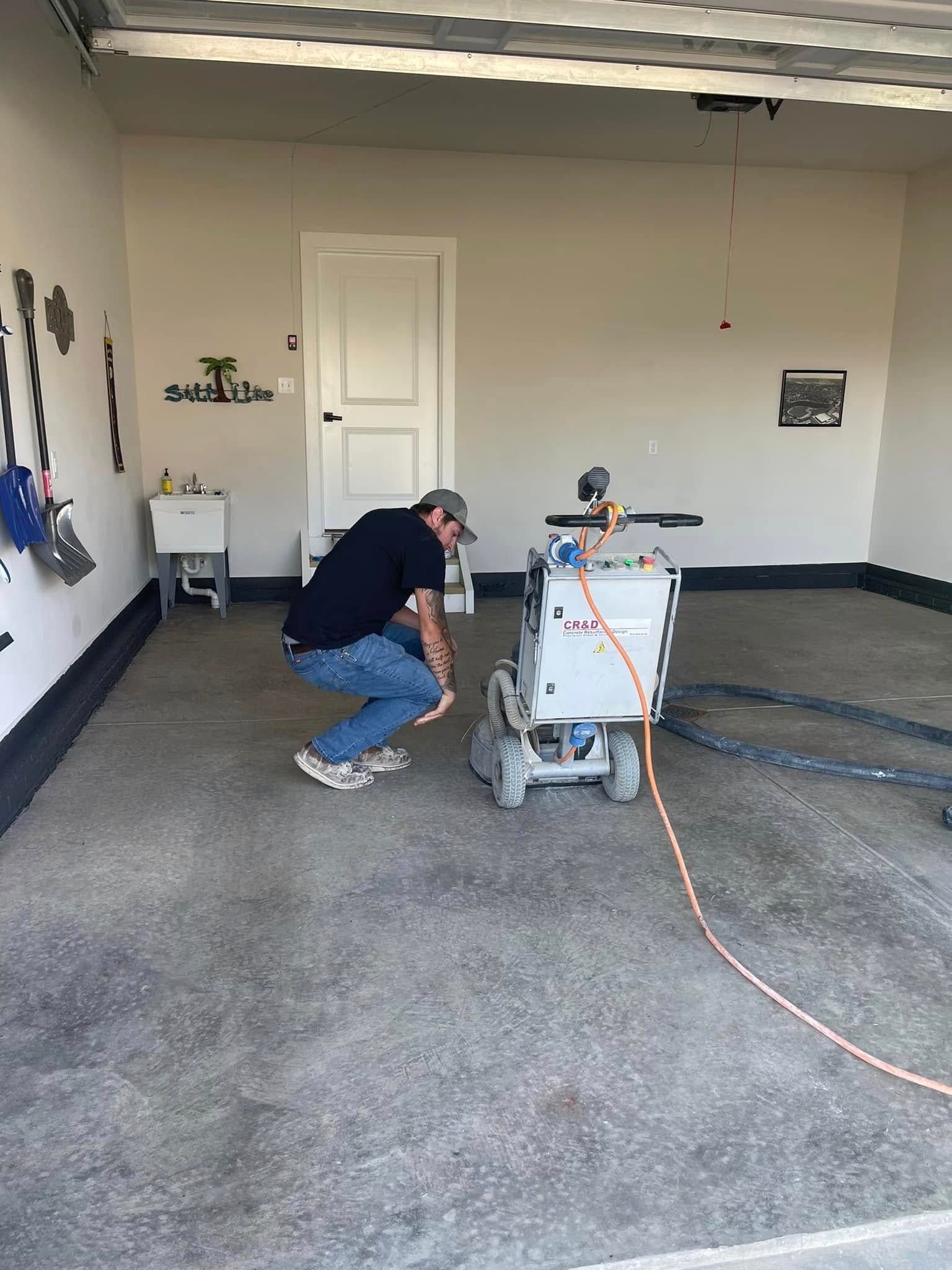 Person crouching beside a carpet-cleaning machine in a garage with gray carpet and an orange hose