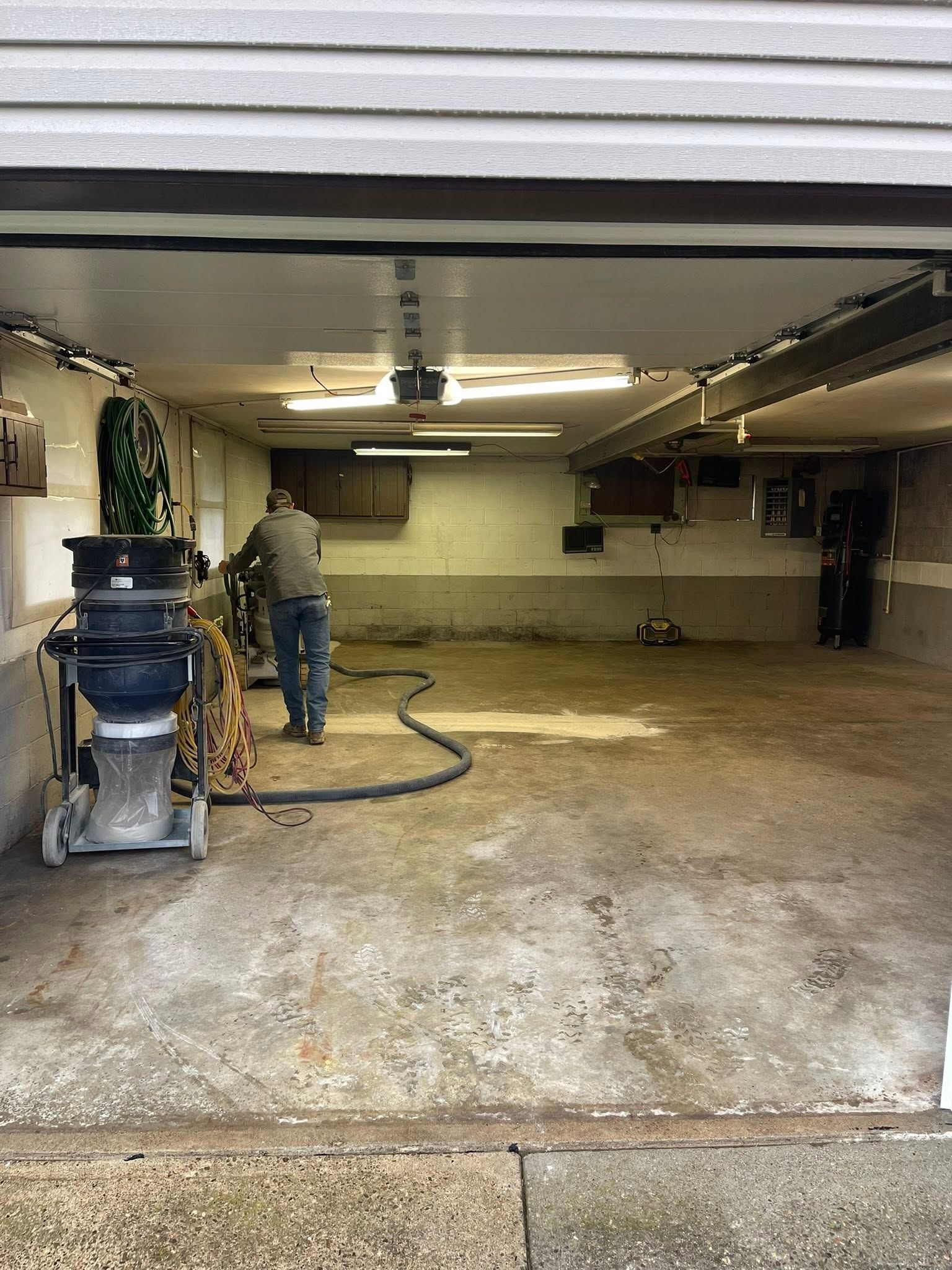 Person power-washing a stained garage floor inside a dim, empty garage