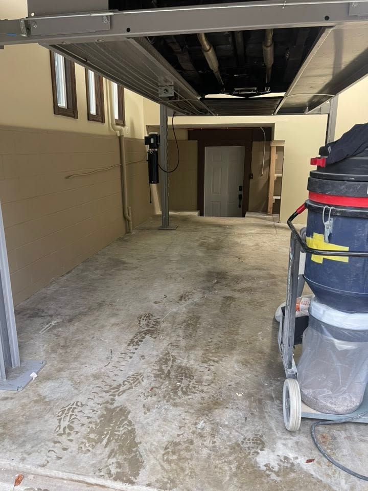 Empty garage or utility bay with concrete floor, overhead beams, and a cleaning cart on the right.