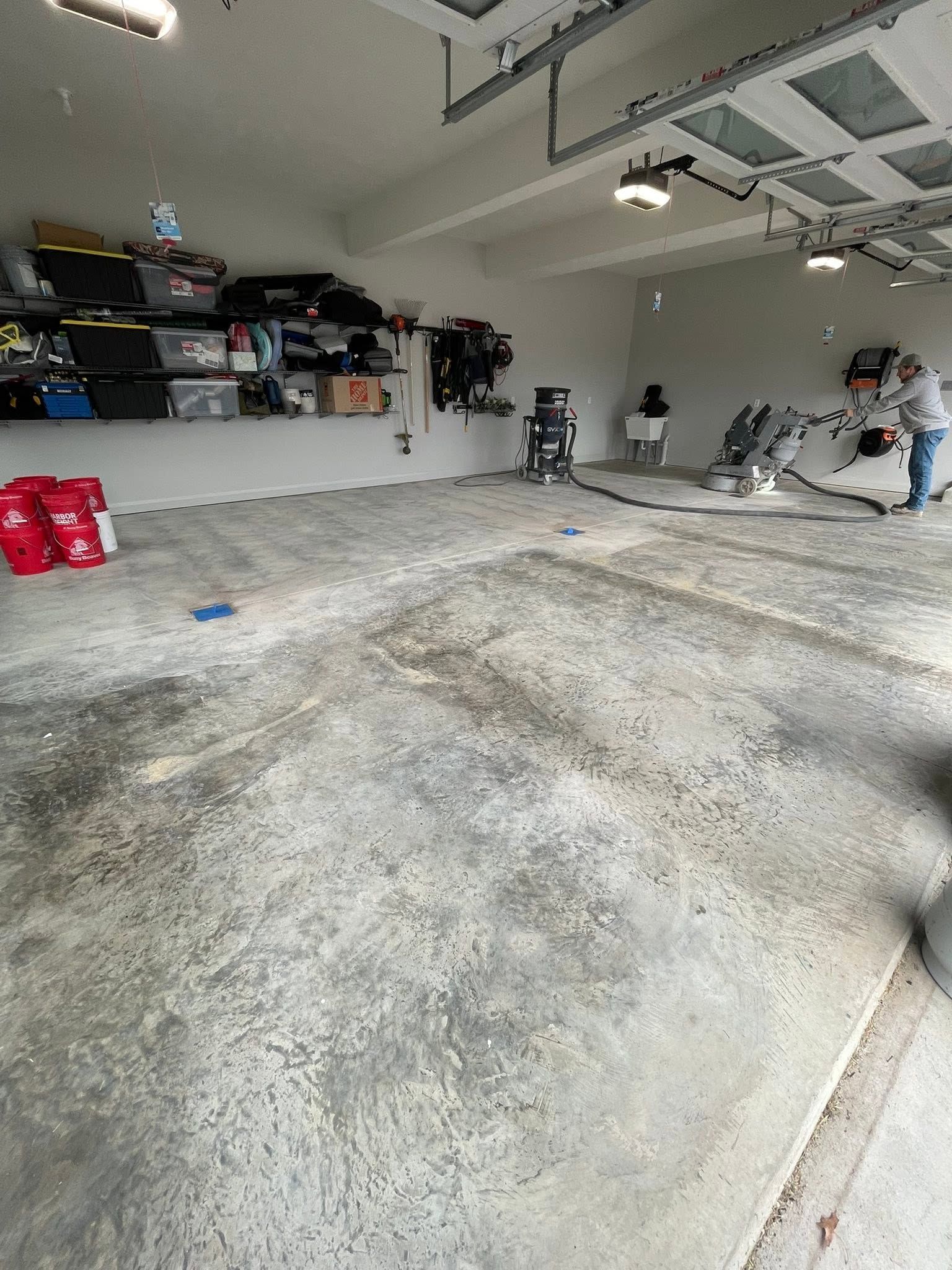 Empty garage with a concrete floor, shelves on the left, and a person working near the back wall.