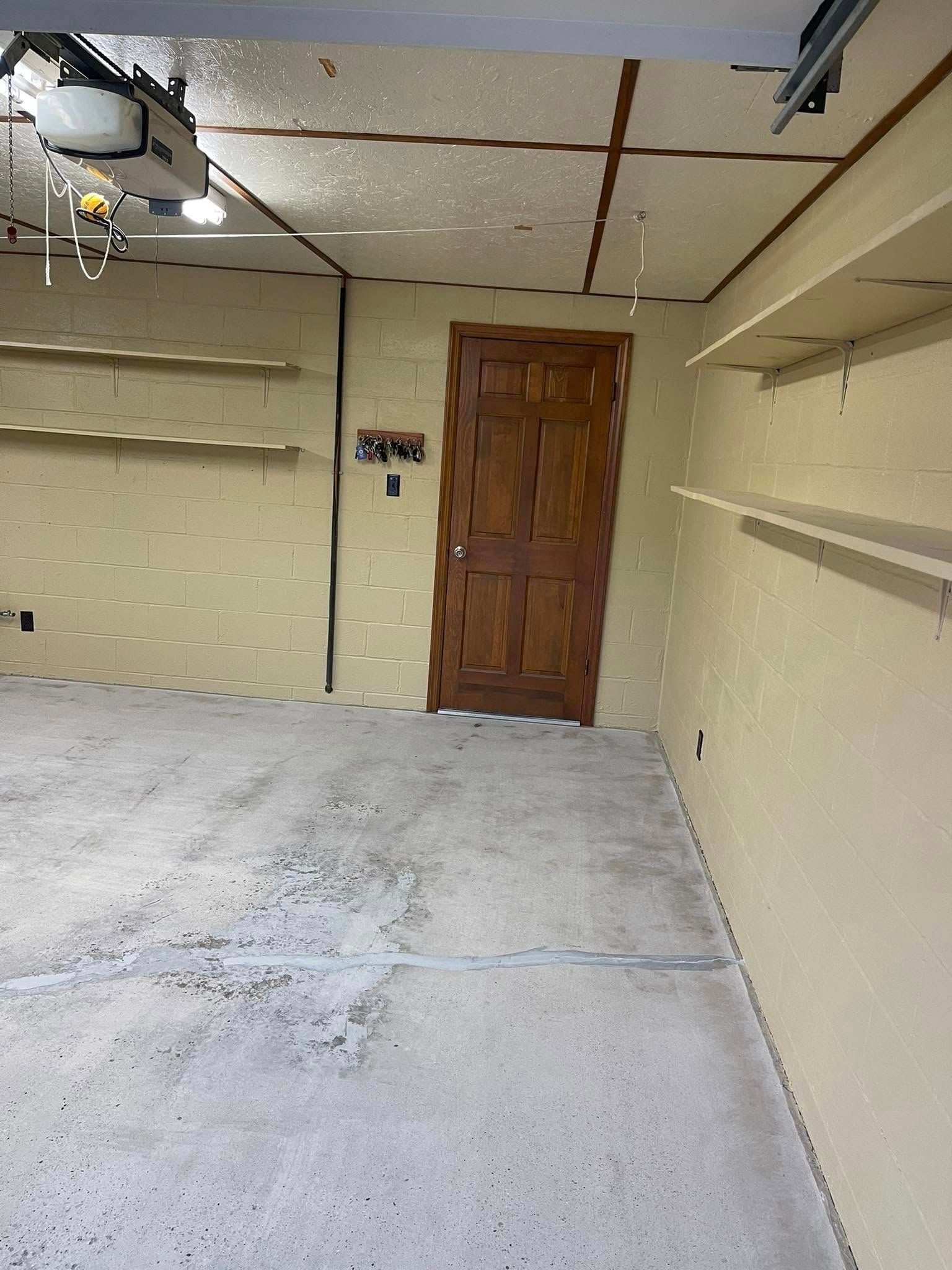 Empty garage with concrete floor, wooden door, and wall shelves