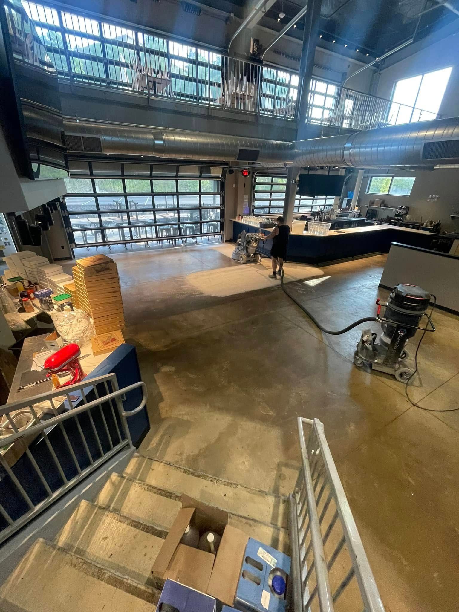 Industrial workshop interior with concrete floor, metal railing, large windows, and machinery on the right.