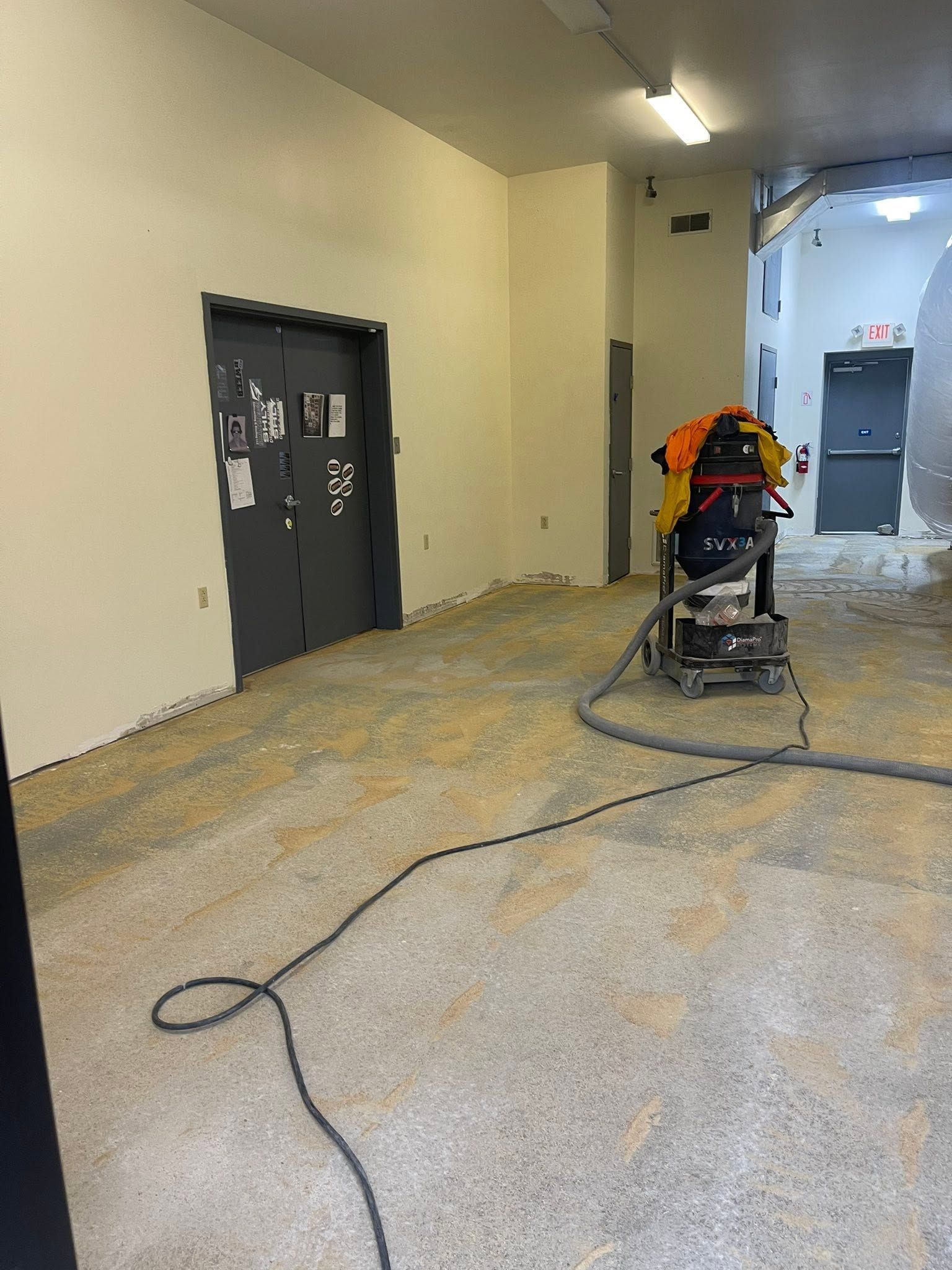 Worker using a floor grinder in a narrow hallway with beige walls and dark doors