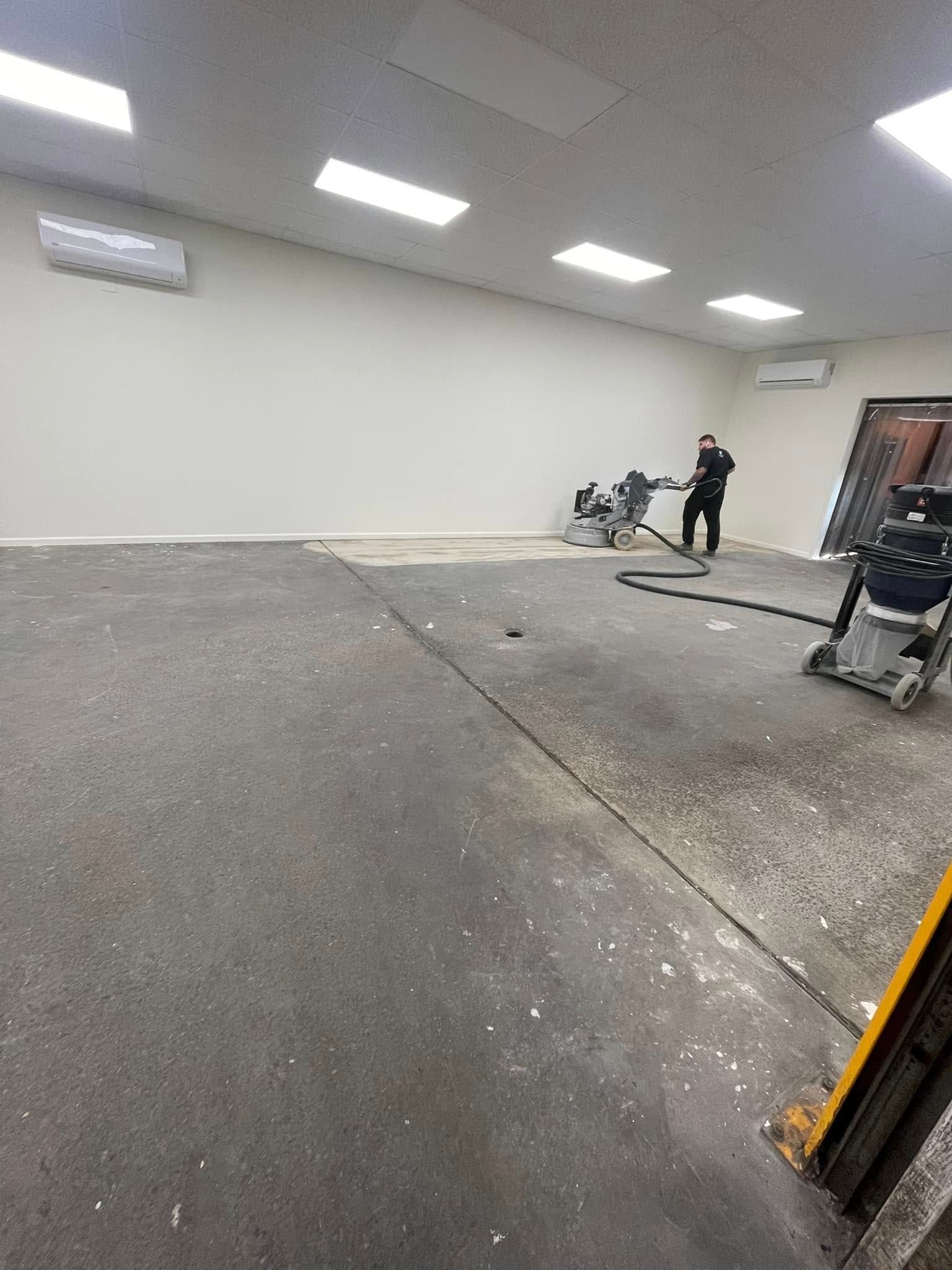 Empty indoor room with gray floor, white walls, and two people near equipment on the right side.
