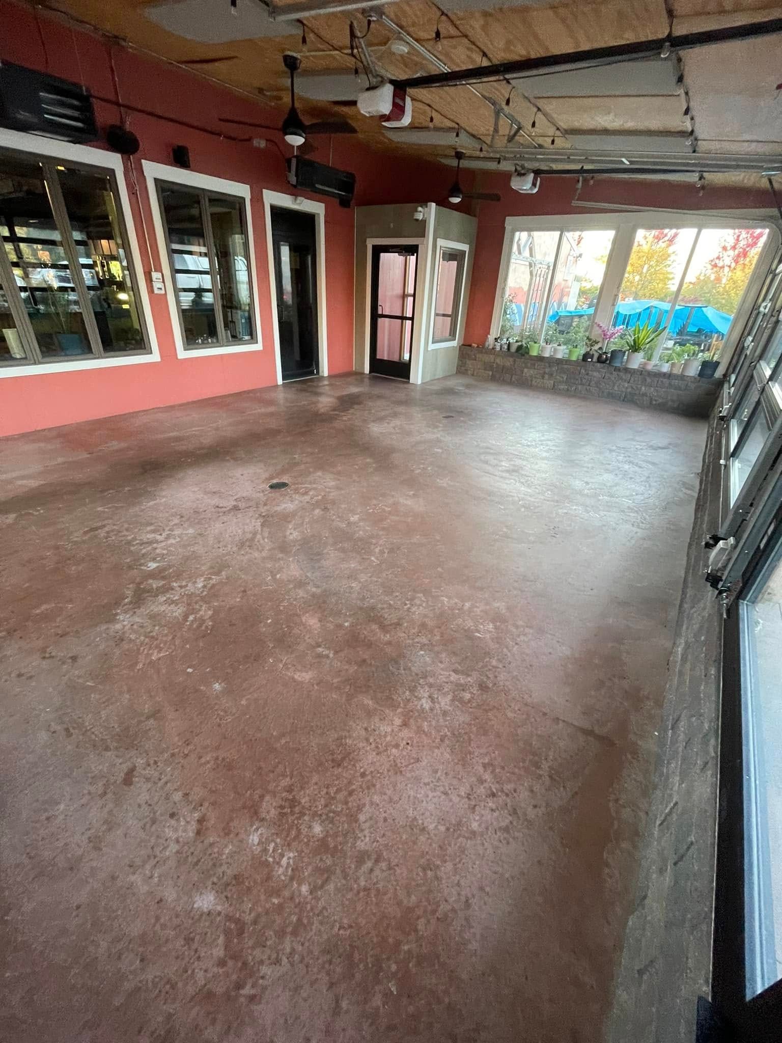 Empty indoor room with pink walls, concrete floor, and large windows letting in daylight