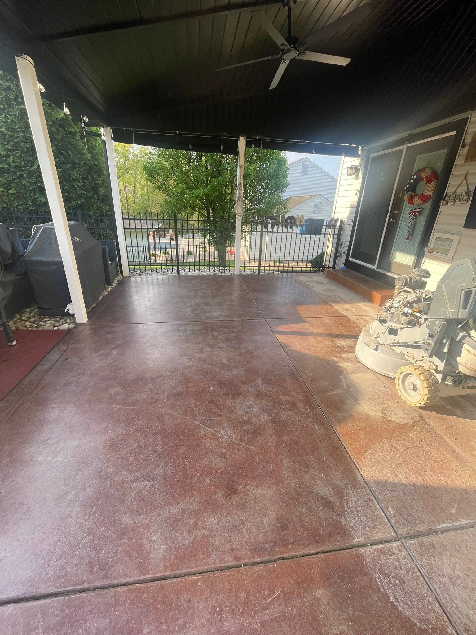Covered porch with red concrete floor, ceiling fan, potted plants, and view of the yard beyond the railing