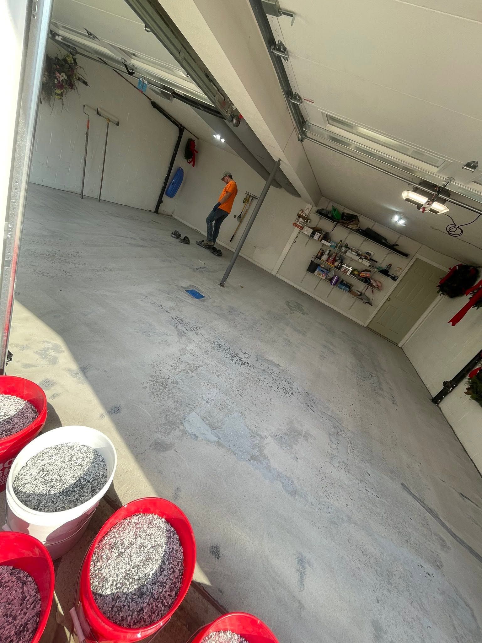 Indoor garage with two workers near a wall, and red bins of gravel in the foreground.