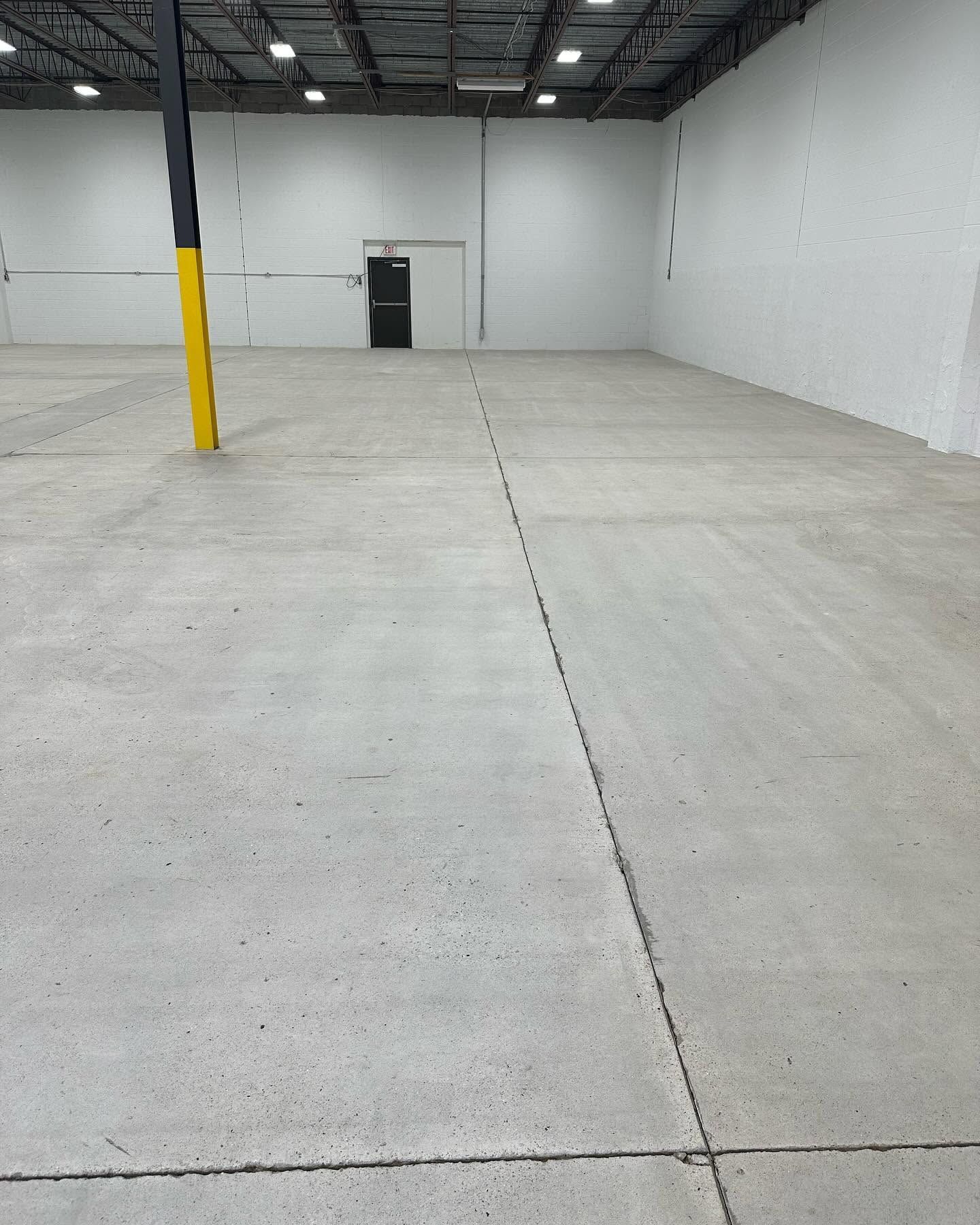 Empty warehouse interior with concrete floor, white walls, and a yellow-black support column.